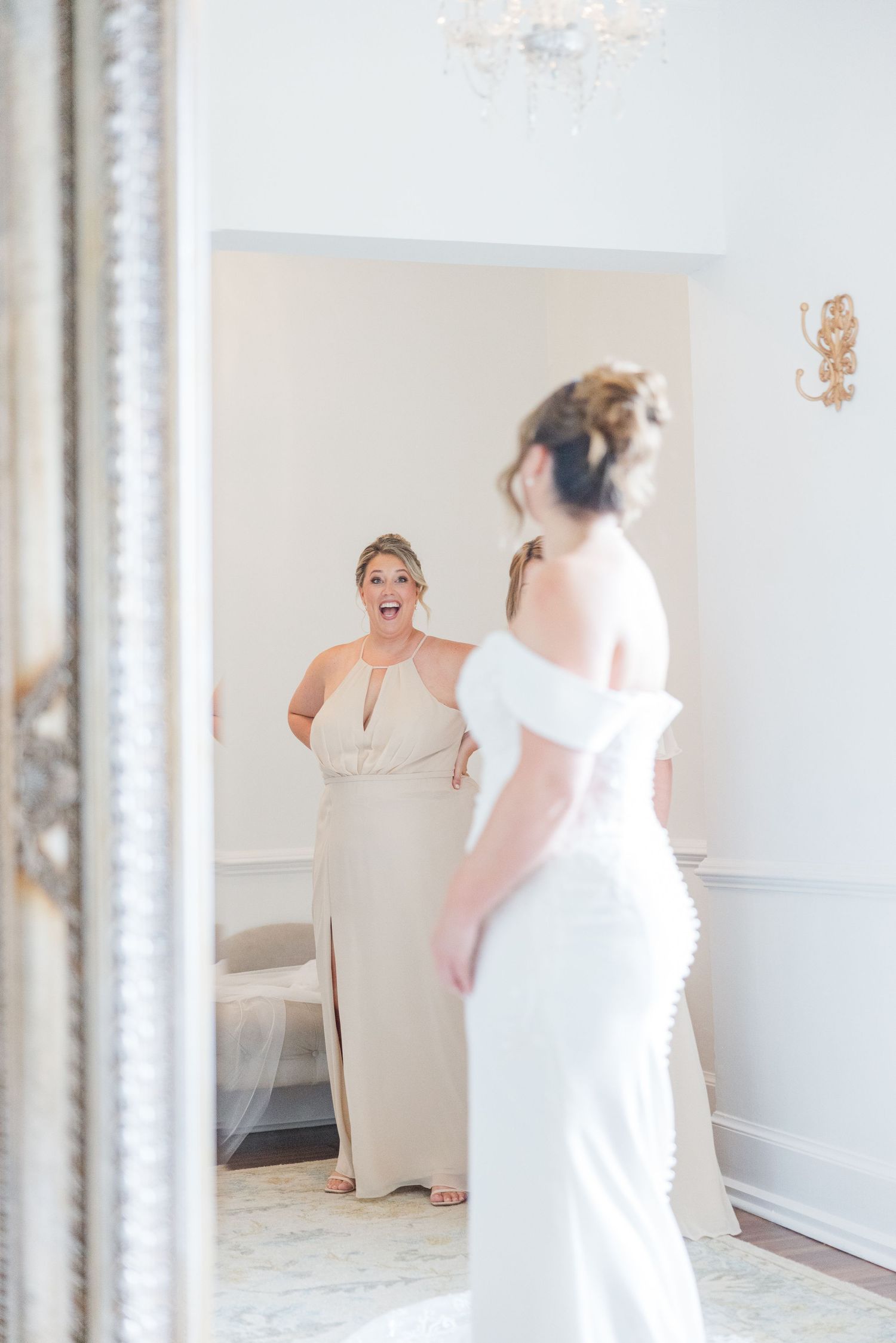 Wedding party members in blush pink dresses getting ready in a bright room with mirrors.