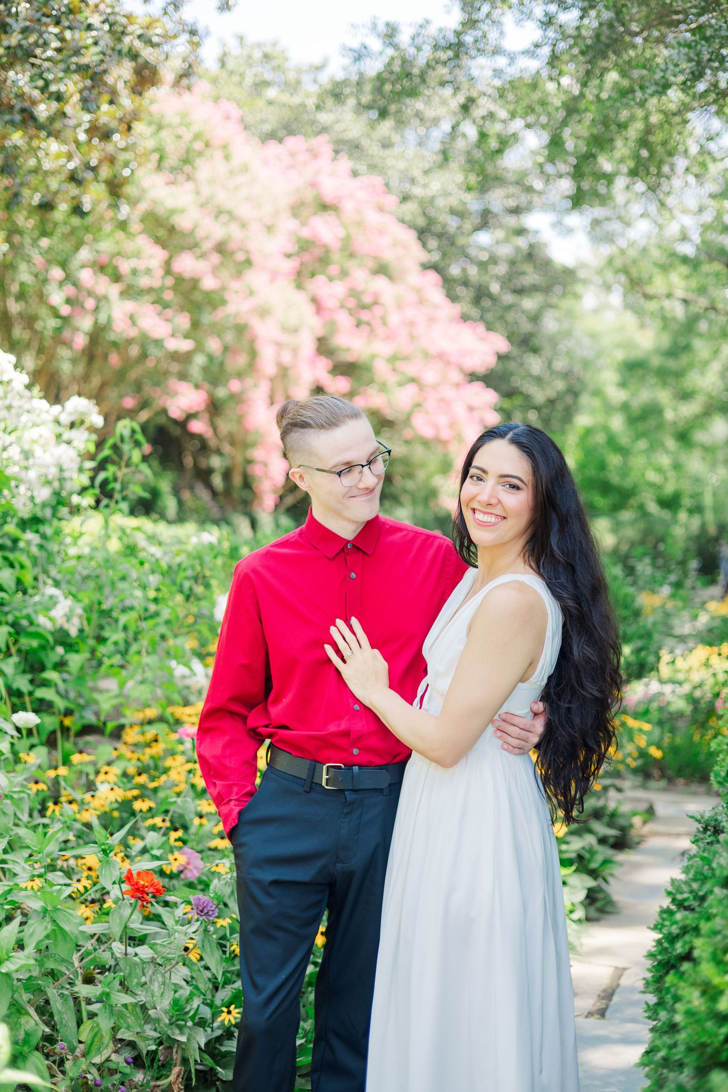 A romantic couple embraces in a lush garden setting with blooming flowers and greenery.