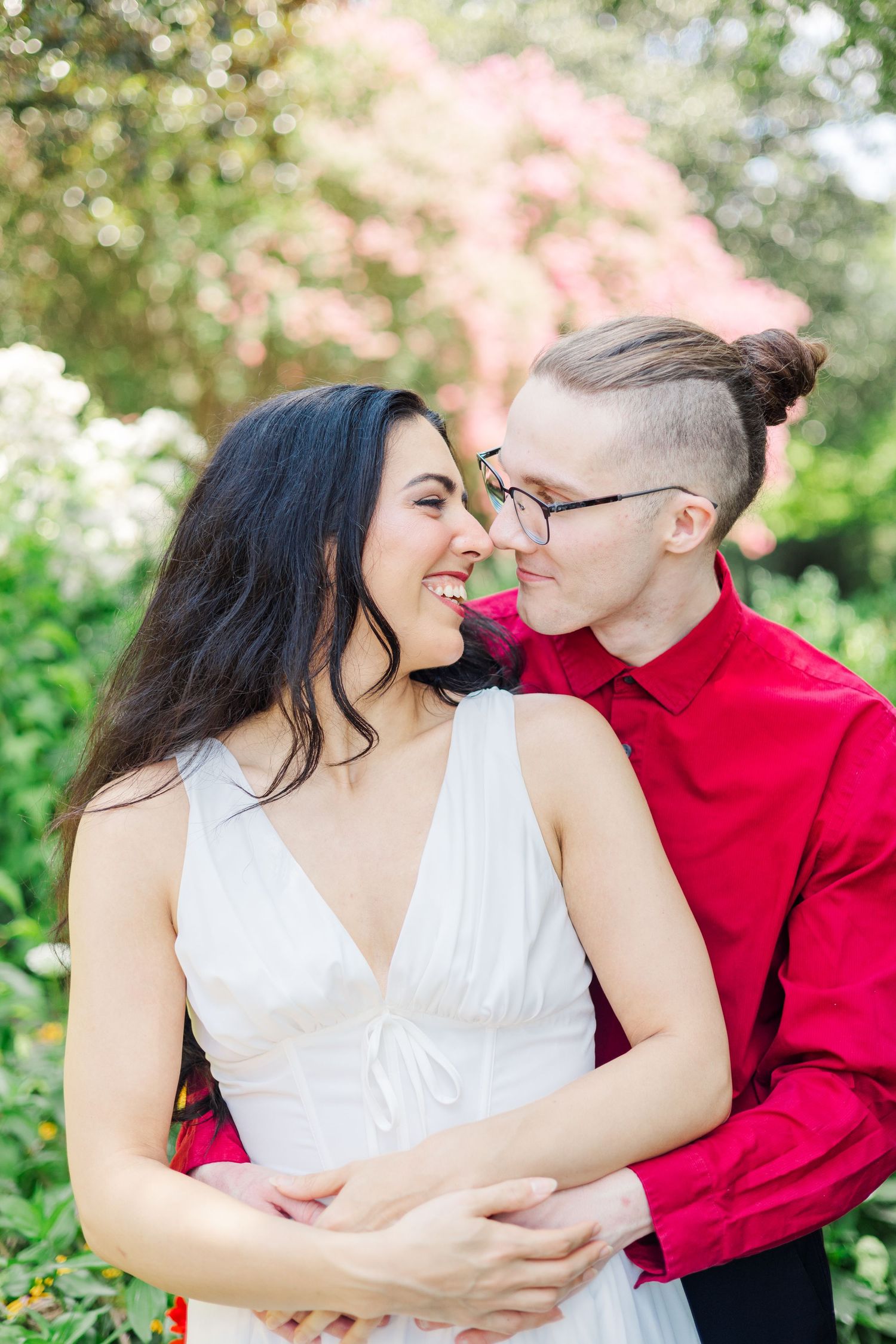 A couple shares intimate moments in a garden setting wearing red and white outfits.