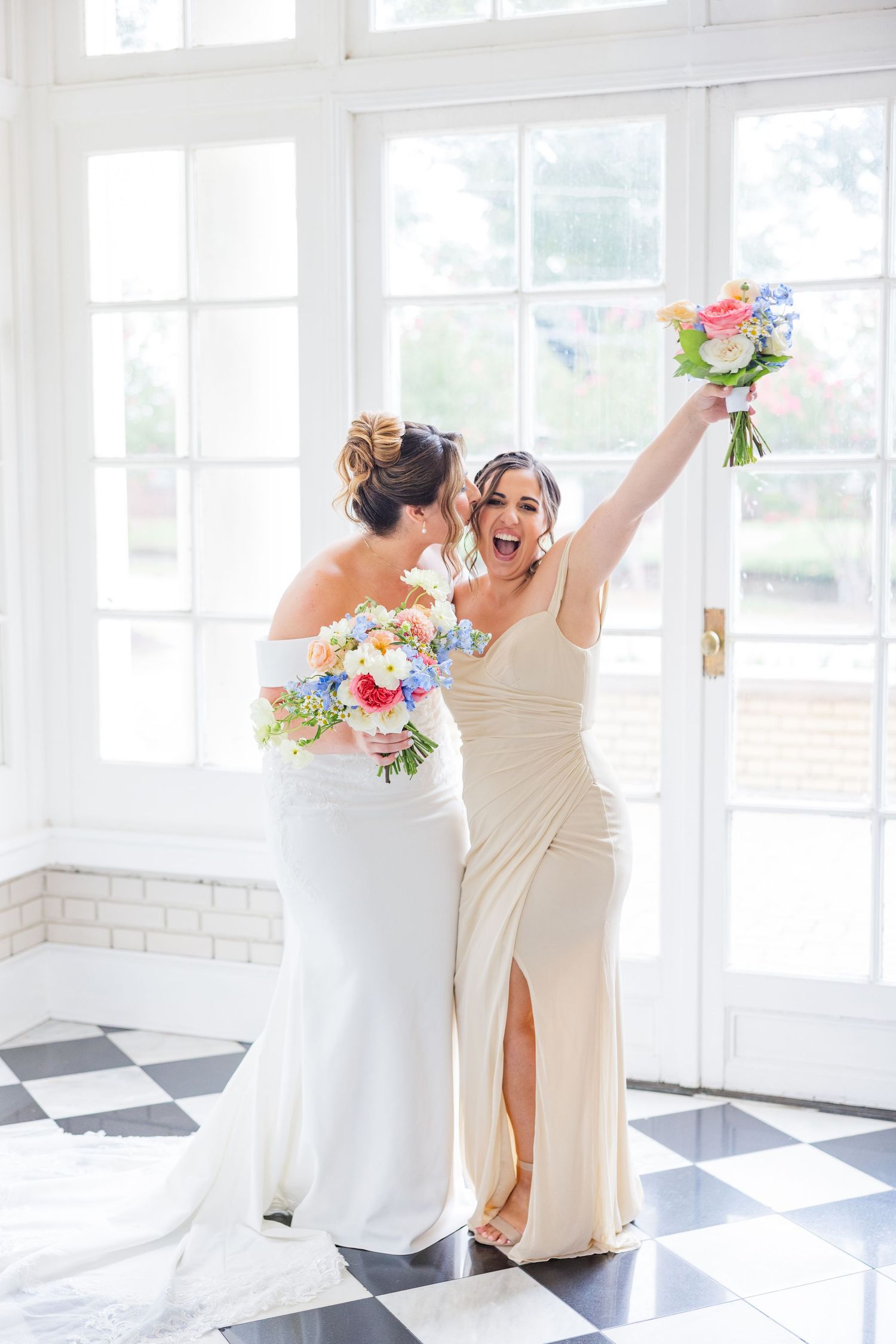 Wedding party members sharing joyful moments in a sun-filled white room with checkered floor.