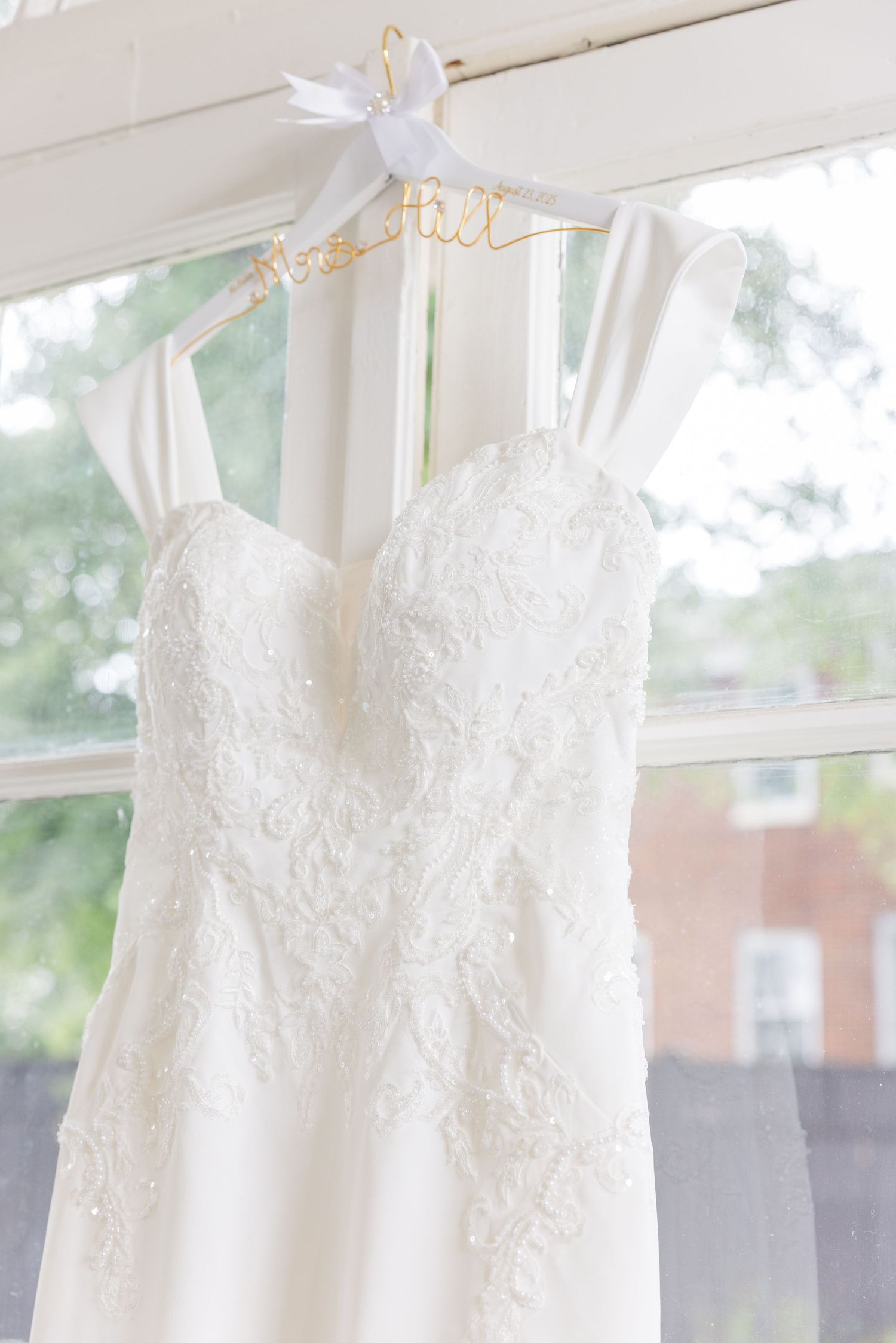 Row of elegant white wedding dresses hanging on display against bright window.