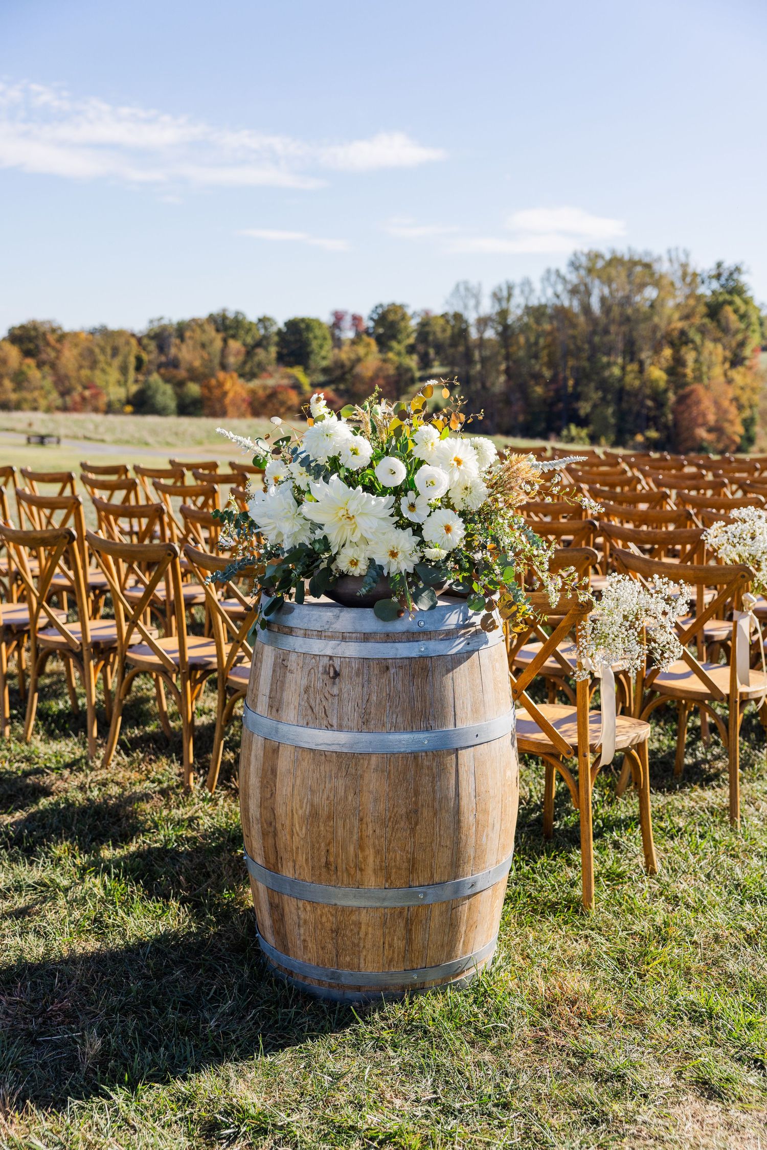 Rustic wedding ceremony setup with wooden barrels and white floral arrangements.