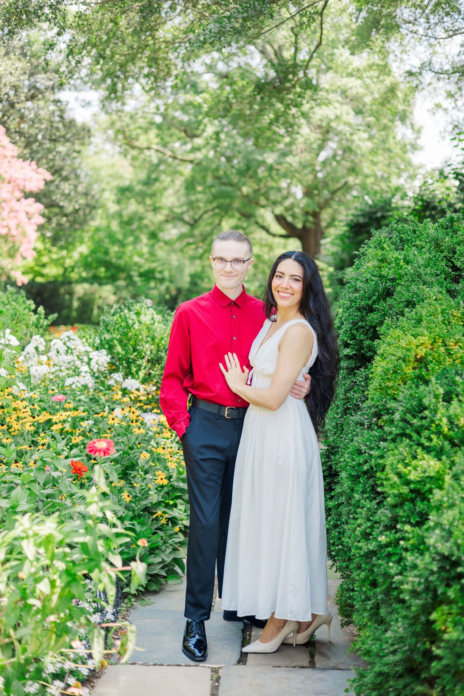 A couple poses together in a lush garden setting with vibrant flowers and greenery.