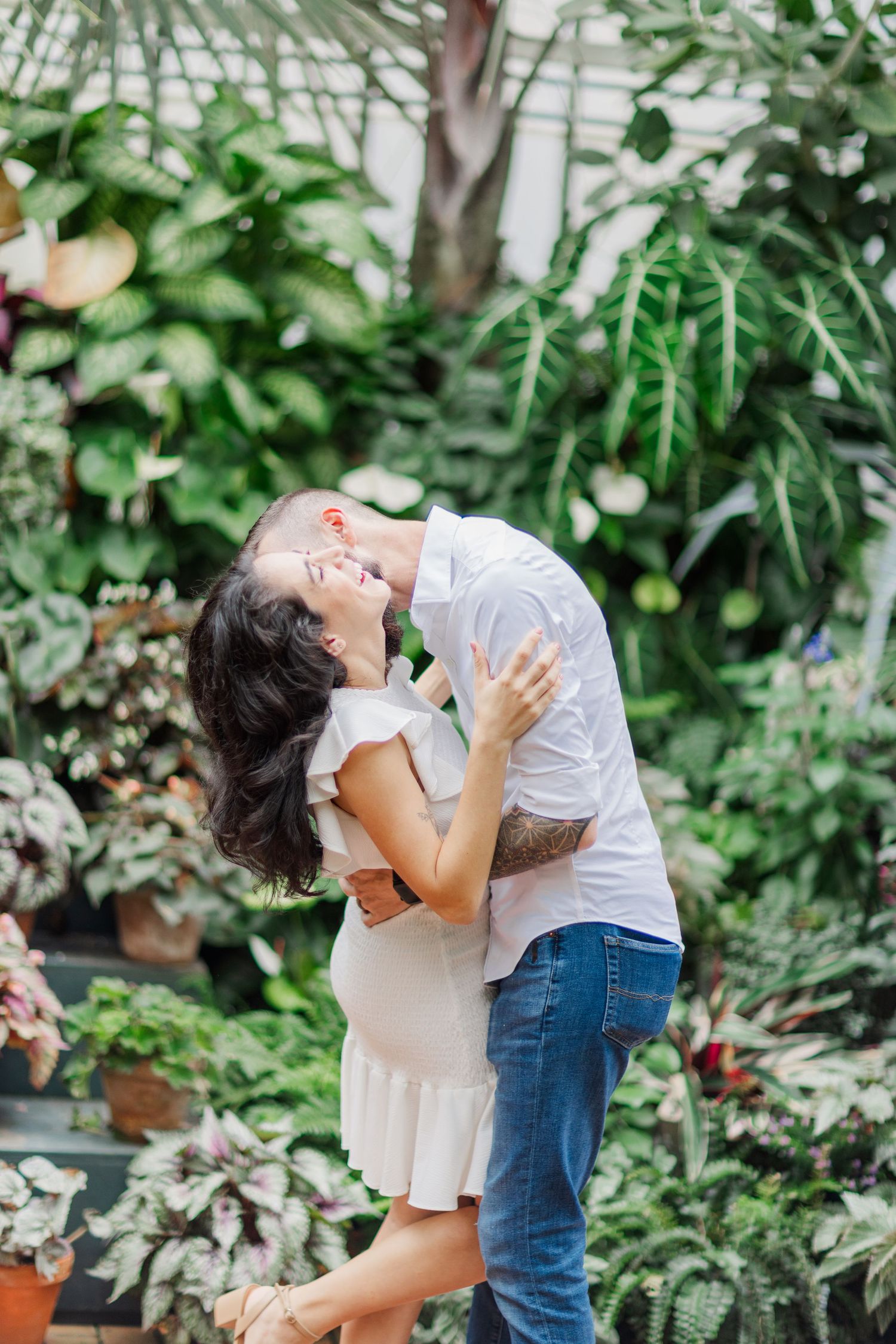 Romantic couple embraces in a lush greenhouse setting surrounded by tropical plants and natural light.