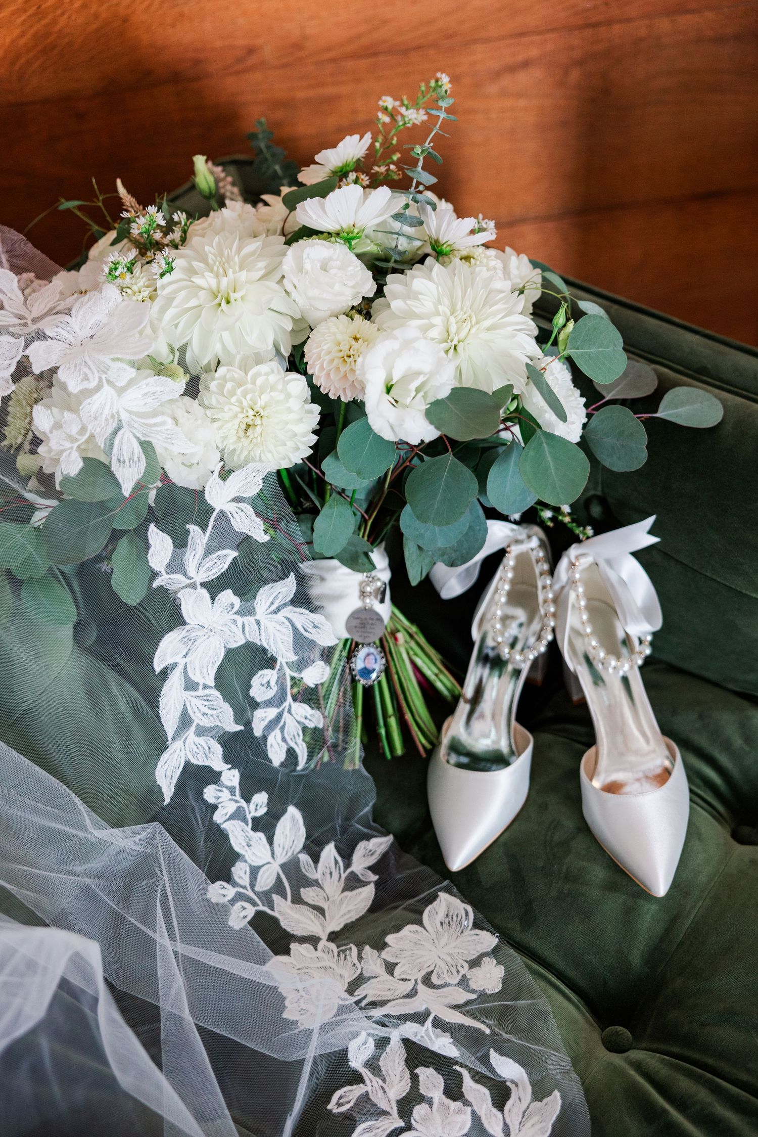 White bridal bouquet with eucalyptus leaves and wedding shoes on dark surface.