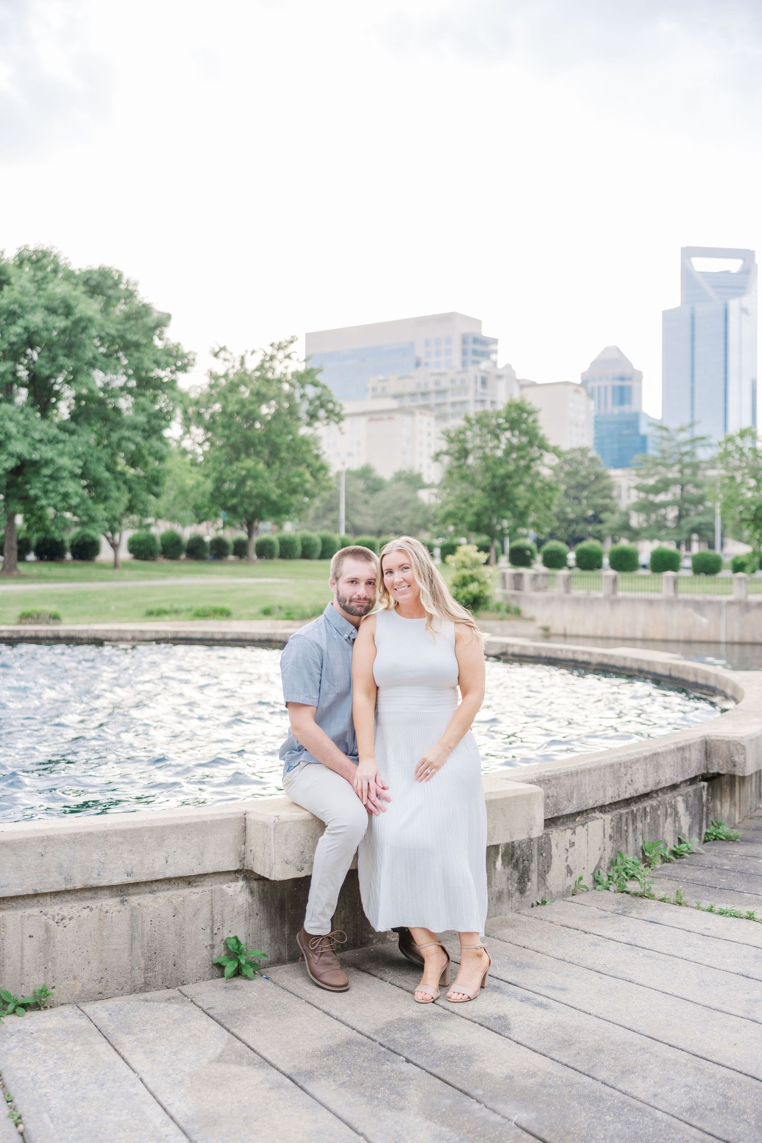 A couple poses for romantic photos along a waterfront promenade with city buildings in the background.