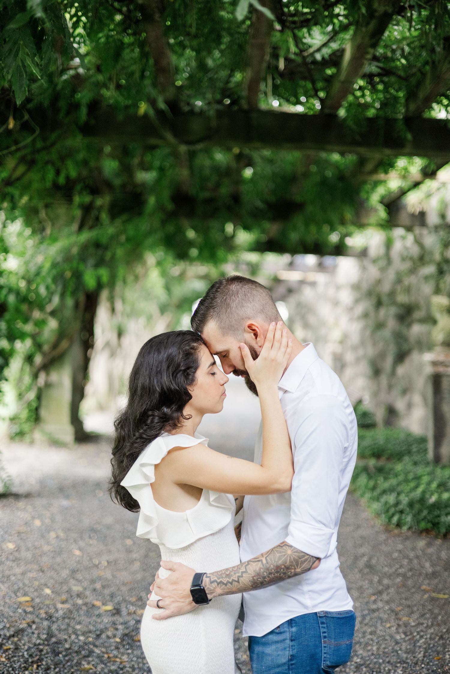 Tender embrace shared between couple on garden path with stone wall backdrop.