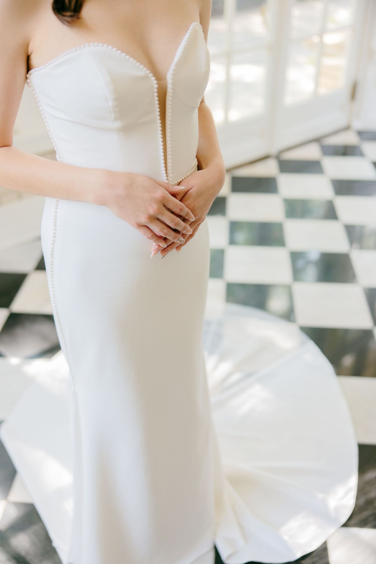 Elegant white wedding dress details showing fitted bodice and flowing fabric against a checkered floor.