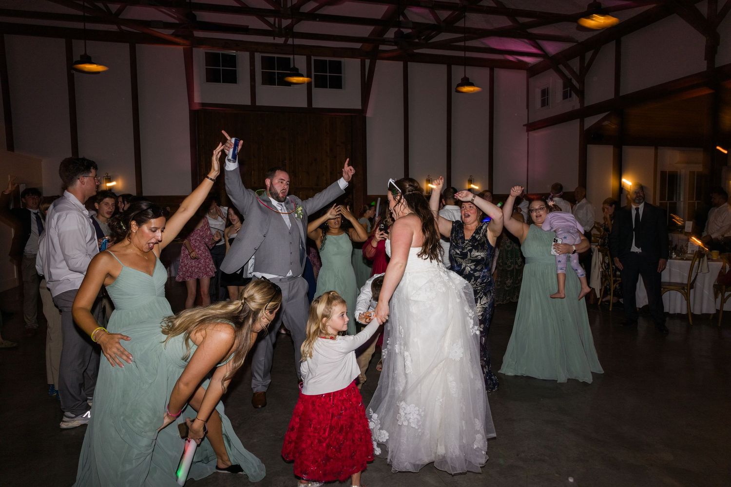 Wedding reception guests dancing and celebrating on a dimly lit dance floor.