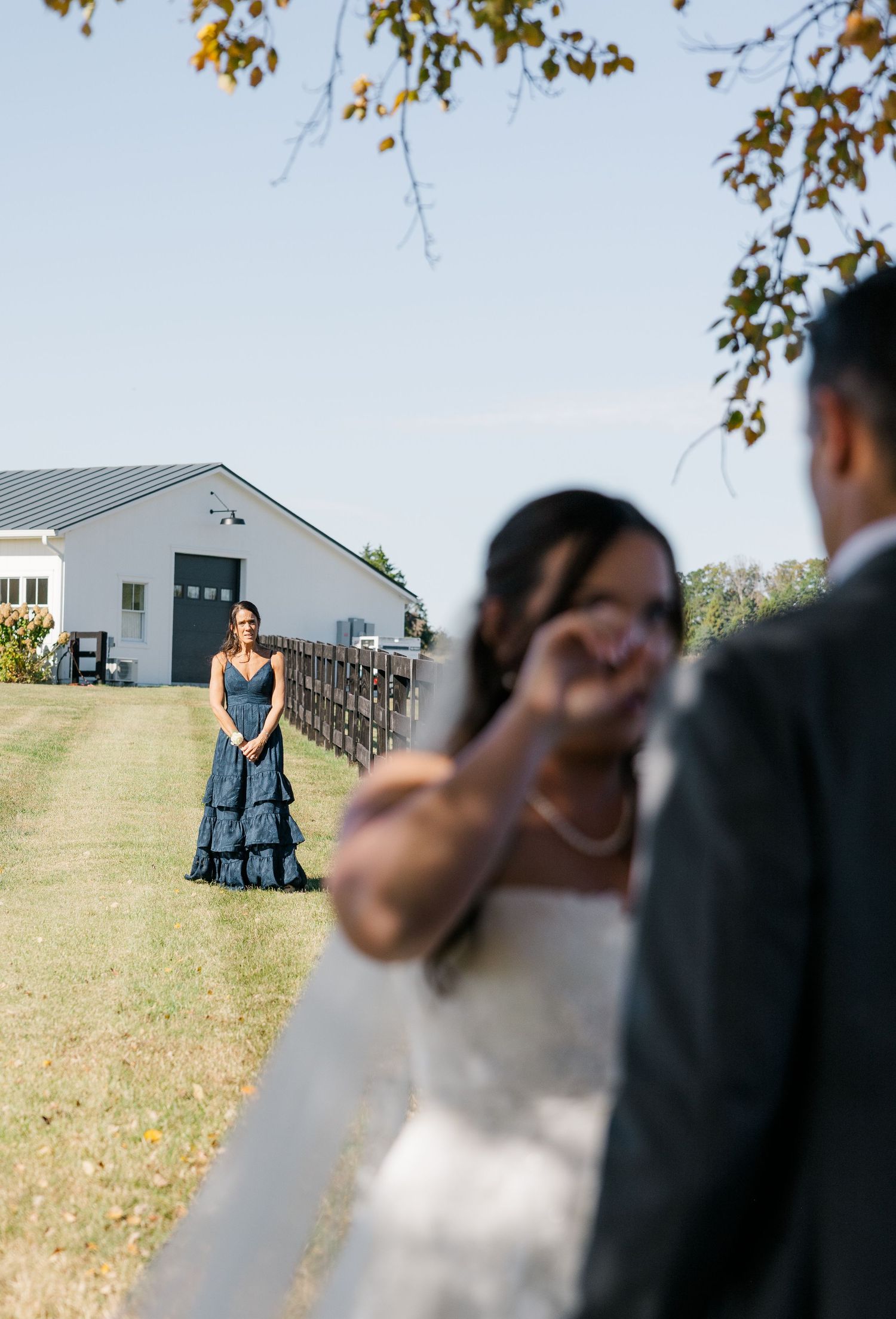 Wedding party members stand in a grassy field with buildings visible in the background.