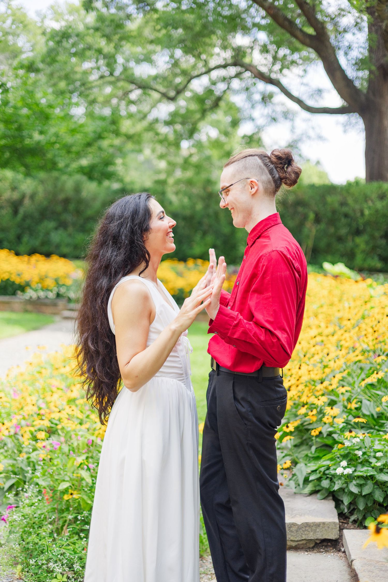 A couple shares a joyful moment in a garden filled with blooming yellow flowers on a sunny day.