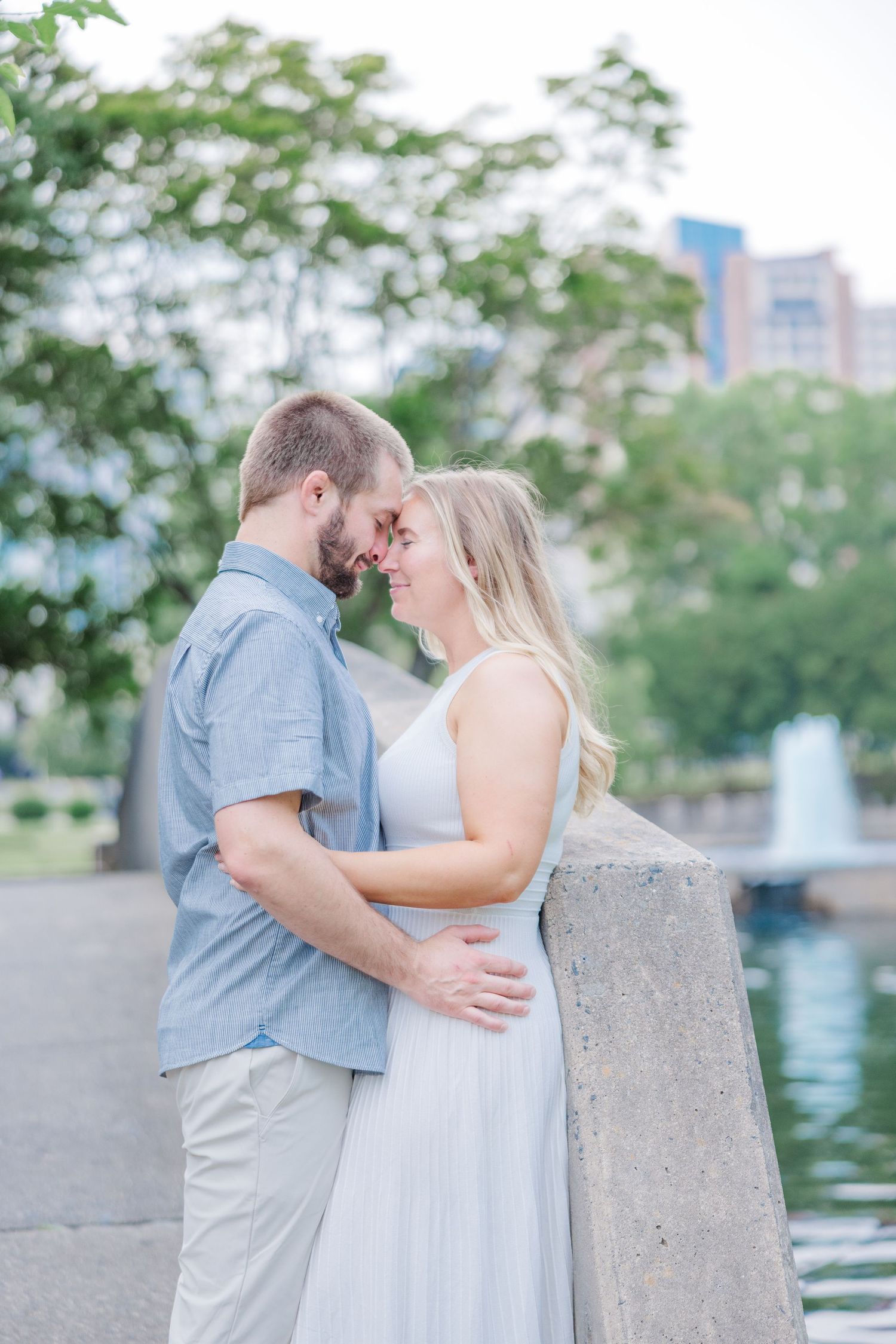 Couple in light summer attire shares intimate moments by a waterfront with city views.