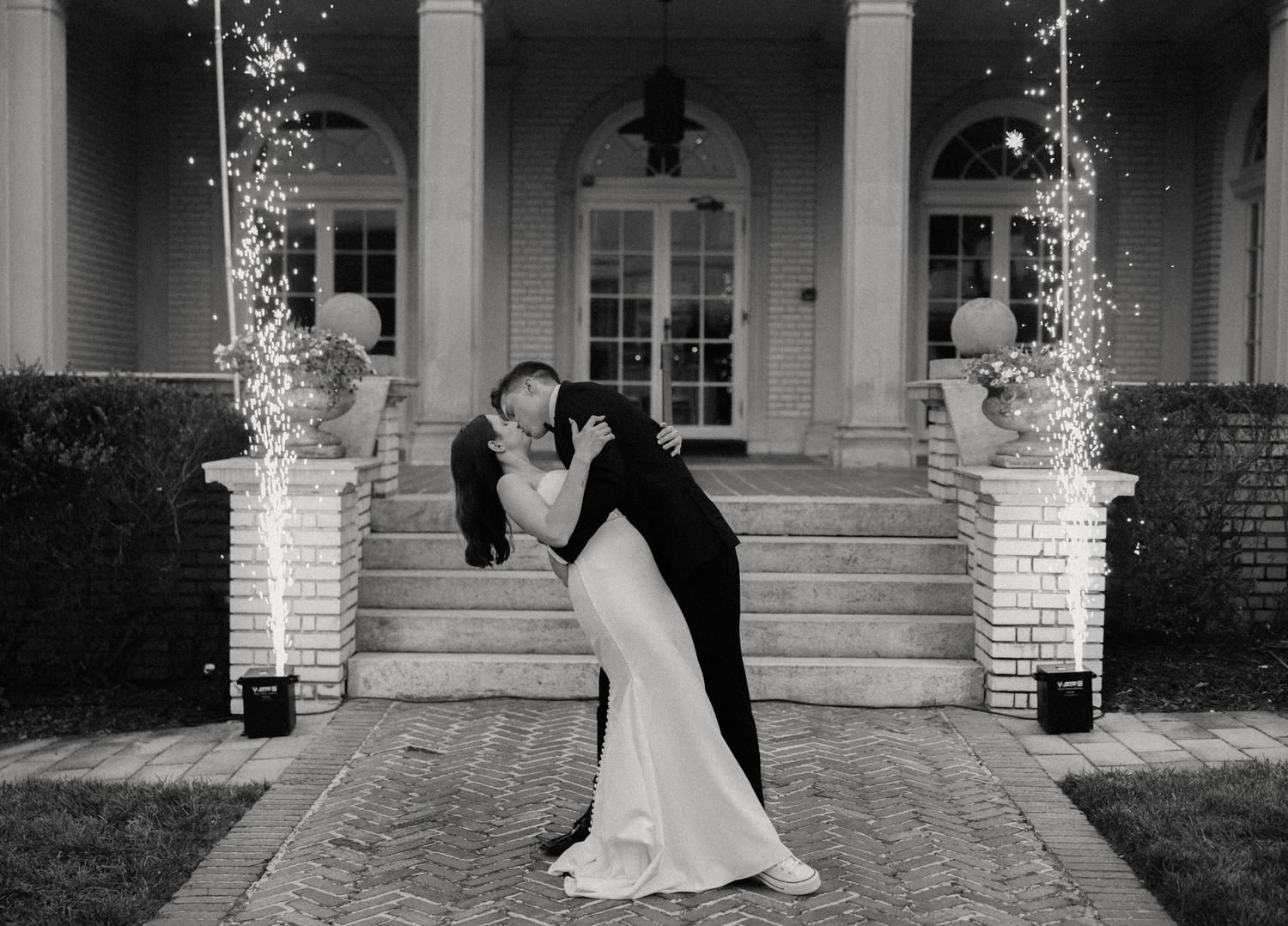 Black and white romantic dip pose on mansion steps with twinkling lights.