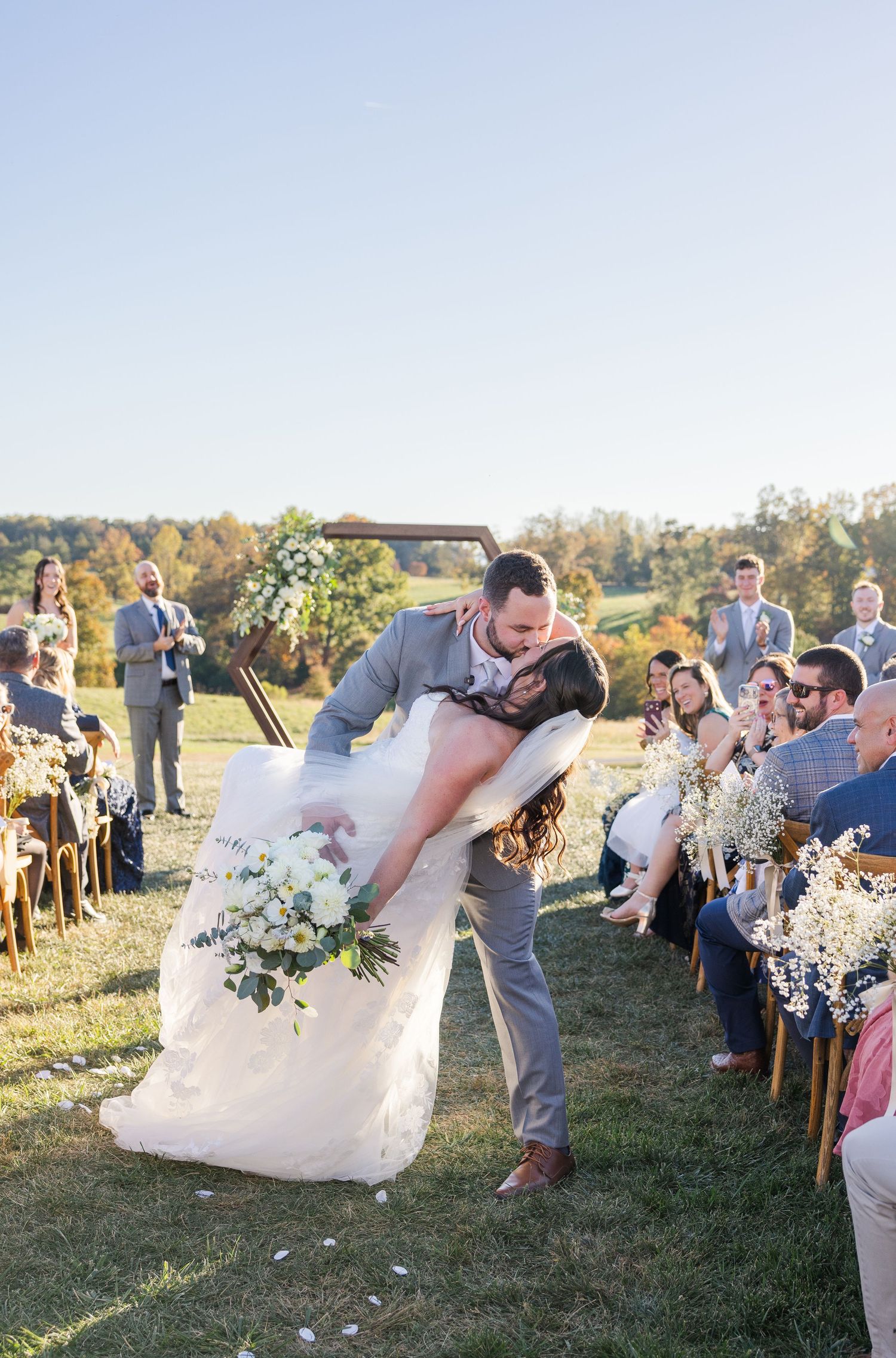 Wedding celebration in a sunny field with guests watching couple's romantic moment.