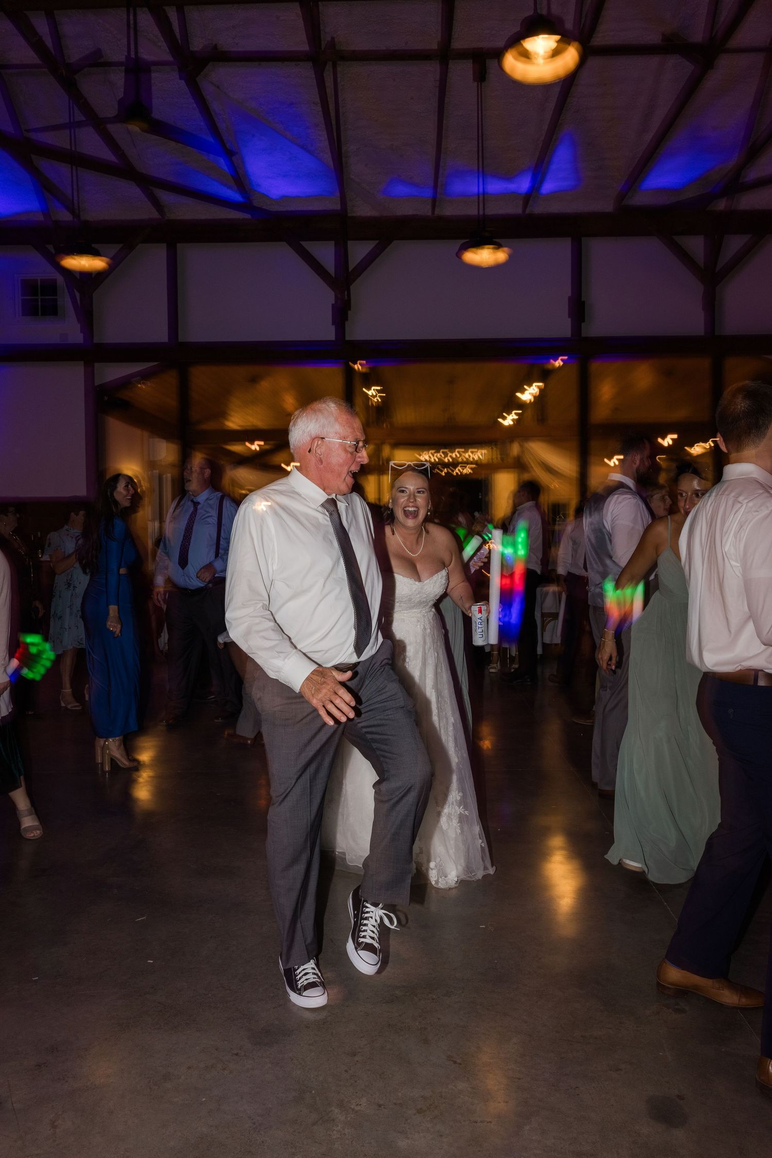 Wedding reception dance floor with colorful lighting and guests dancing in a rustic venue.
