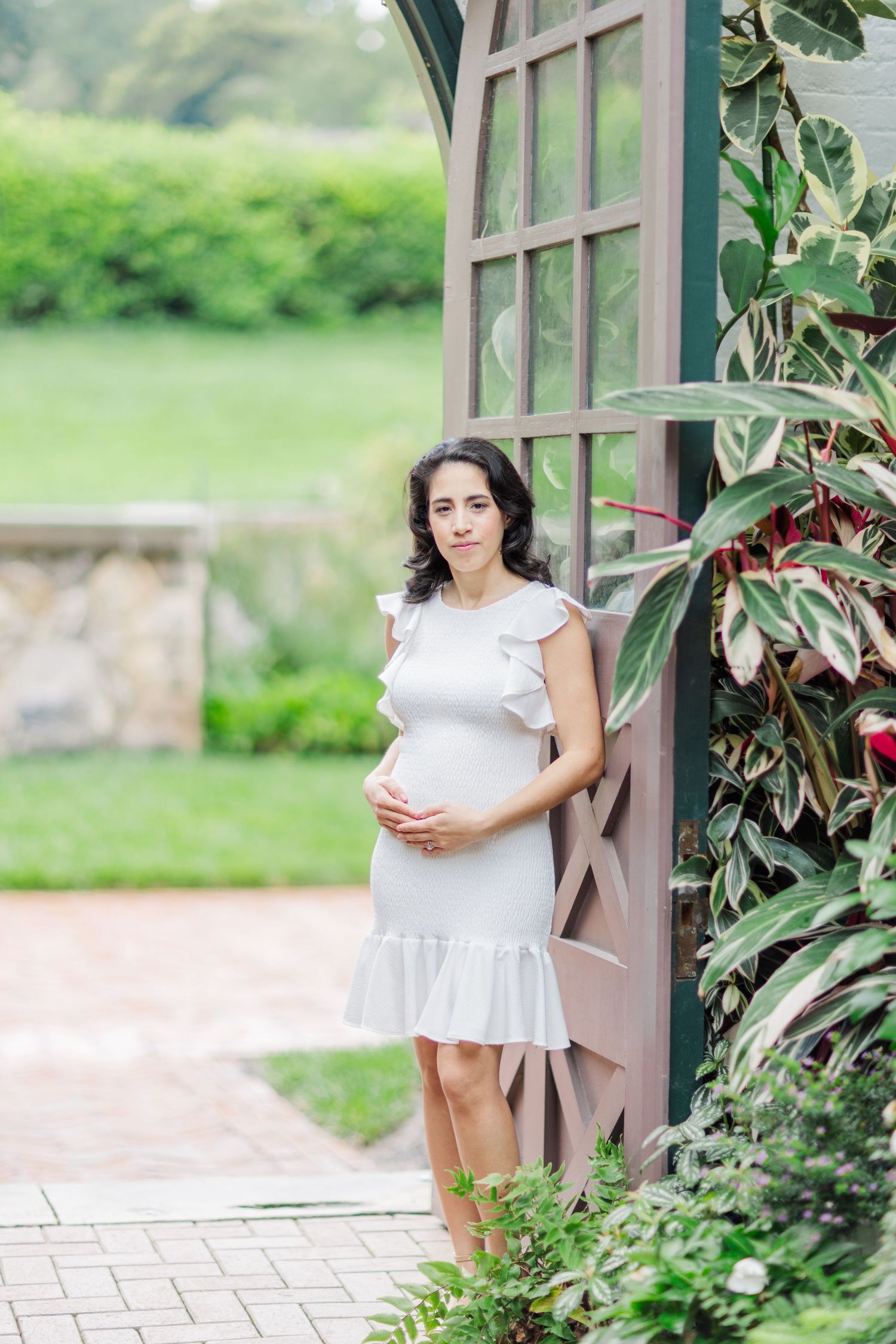 A white dress flows elegantly against a backdrop of green foliage and architectural details.