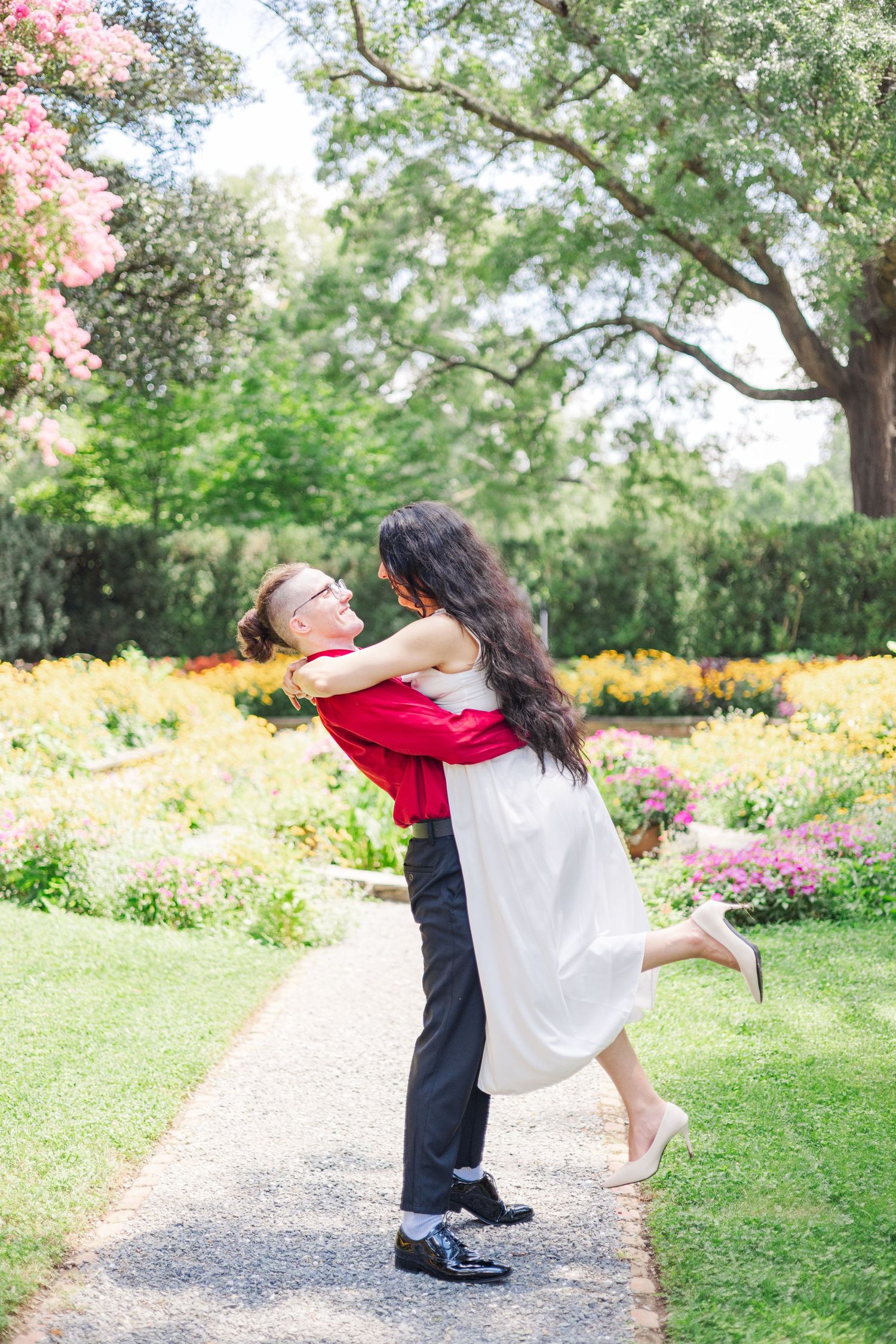 A couple performs a romantic dip pose on a garden path surrounded by blooming flowers.