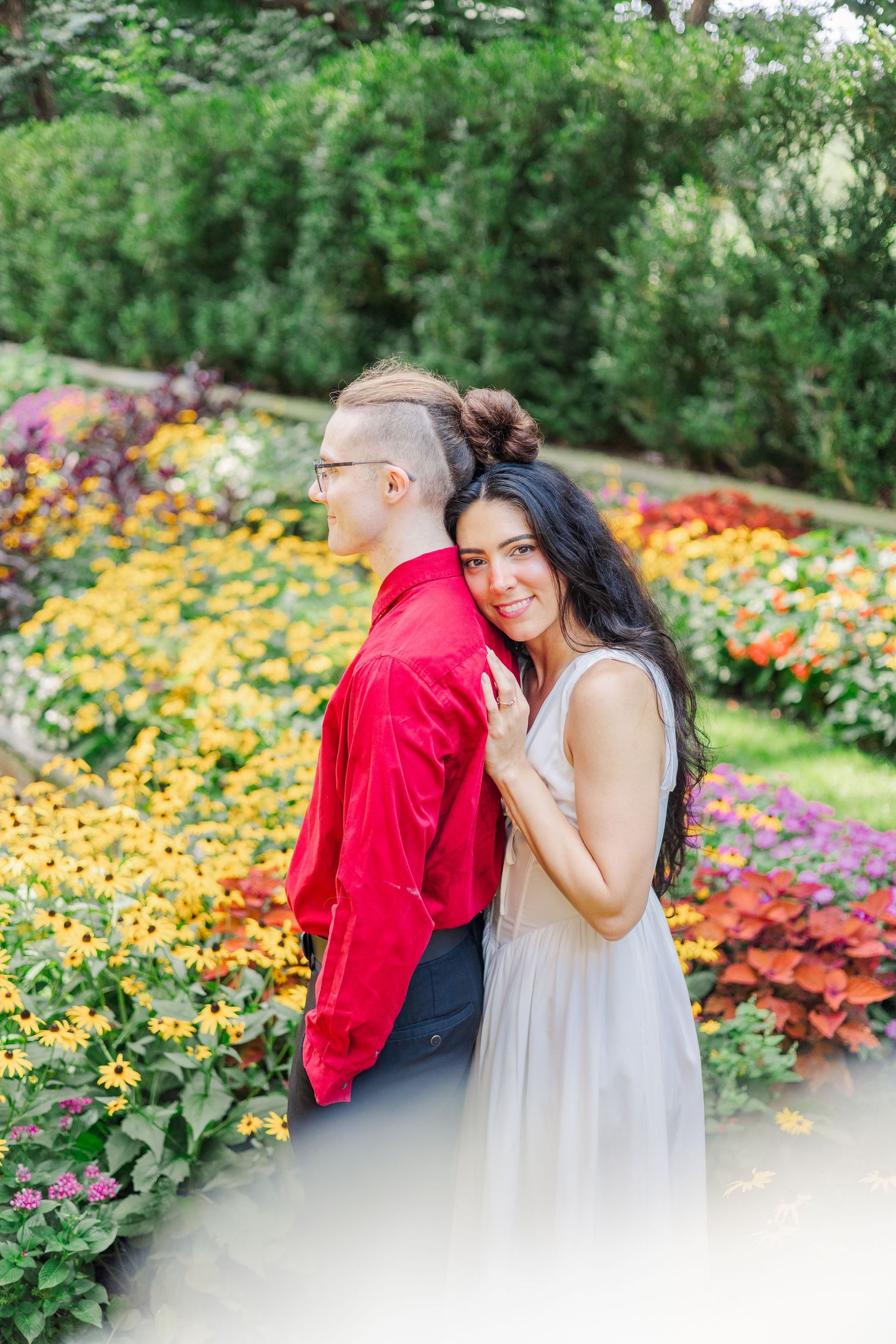 Two people share a joyful moment together in a vibrant garden filled with colorful flowers and greenery.