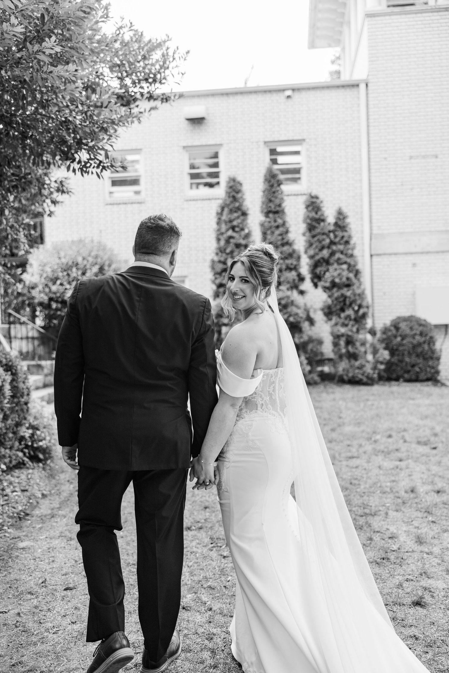 Black and white outdoor wedding photo capturing intimate moment on garden path.