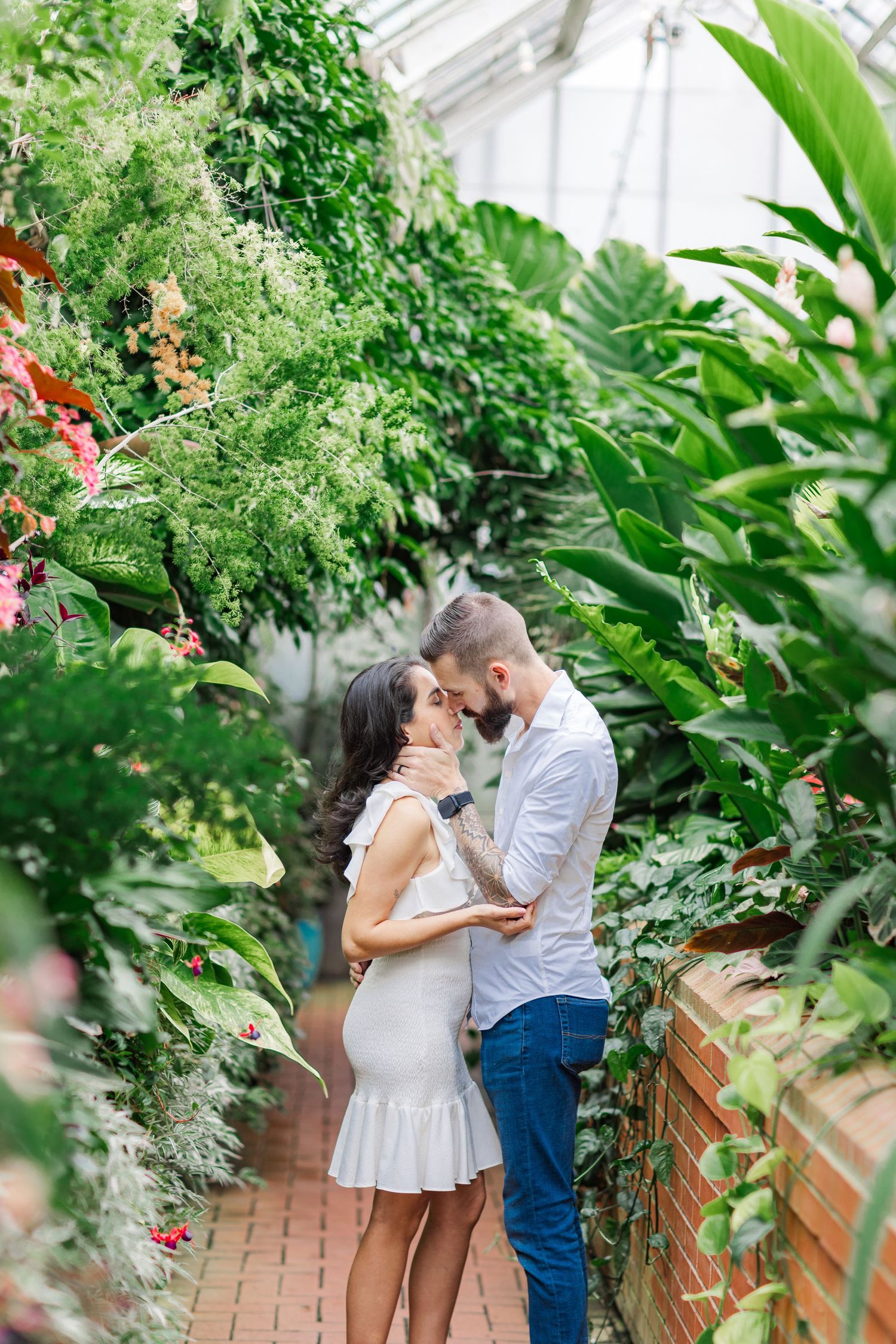 Greenhouse romance captured among tropical plants and red brick walls.