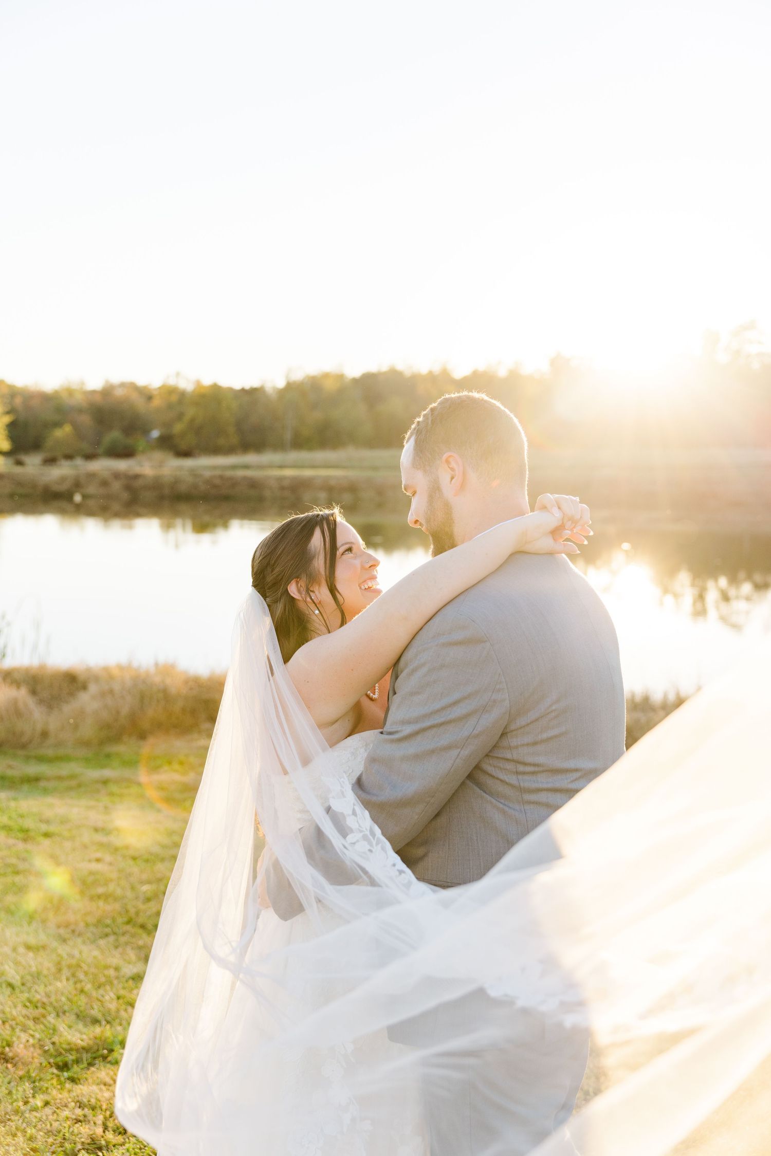 Romantic sunset wedding portraits with flowing veil by a lakeside.