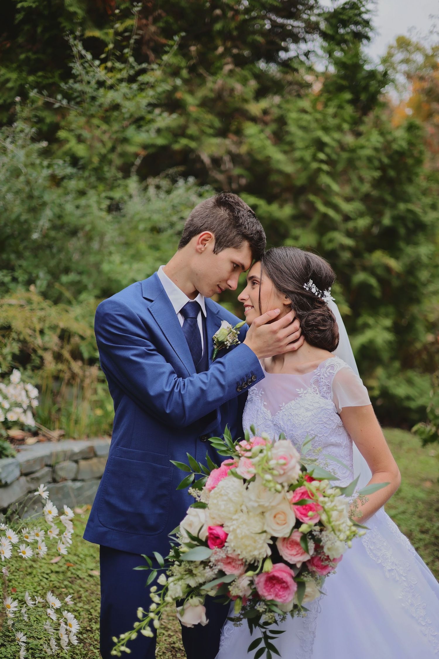 Romantic garden wedding scene with couple in blue suit and white dress among flowers.