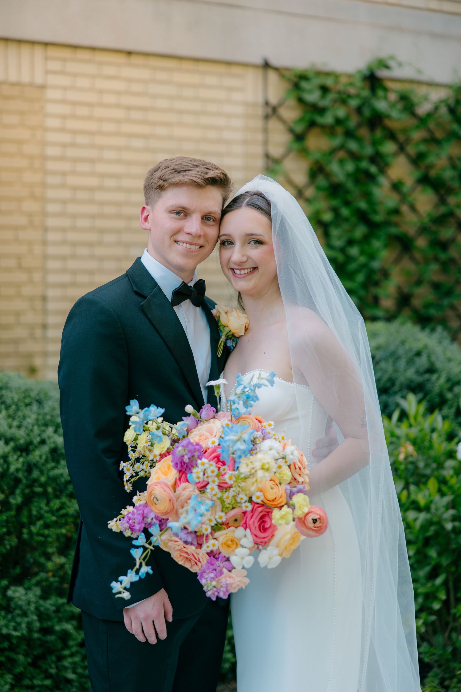 Wedding couple in a garden setting with a vibrant colorful bouquet of mixed flowers.