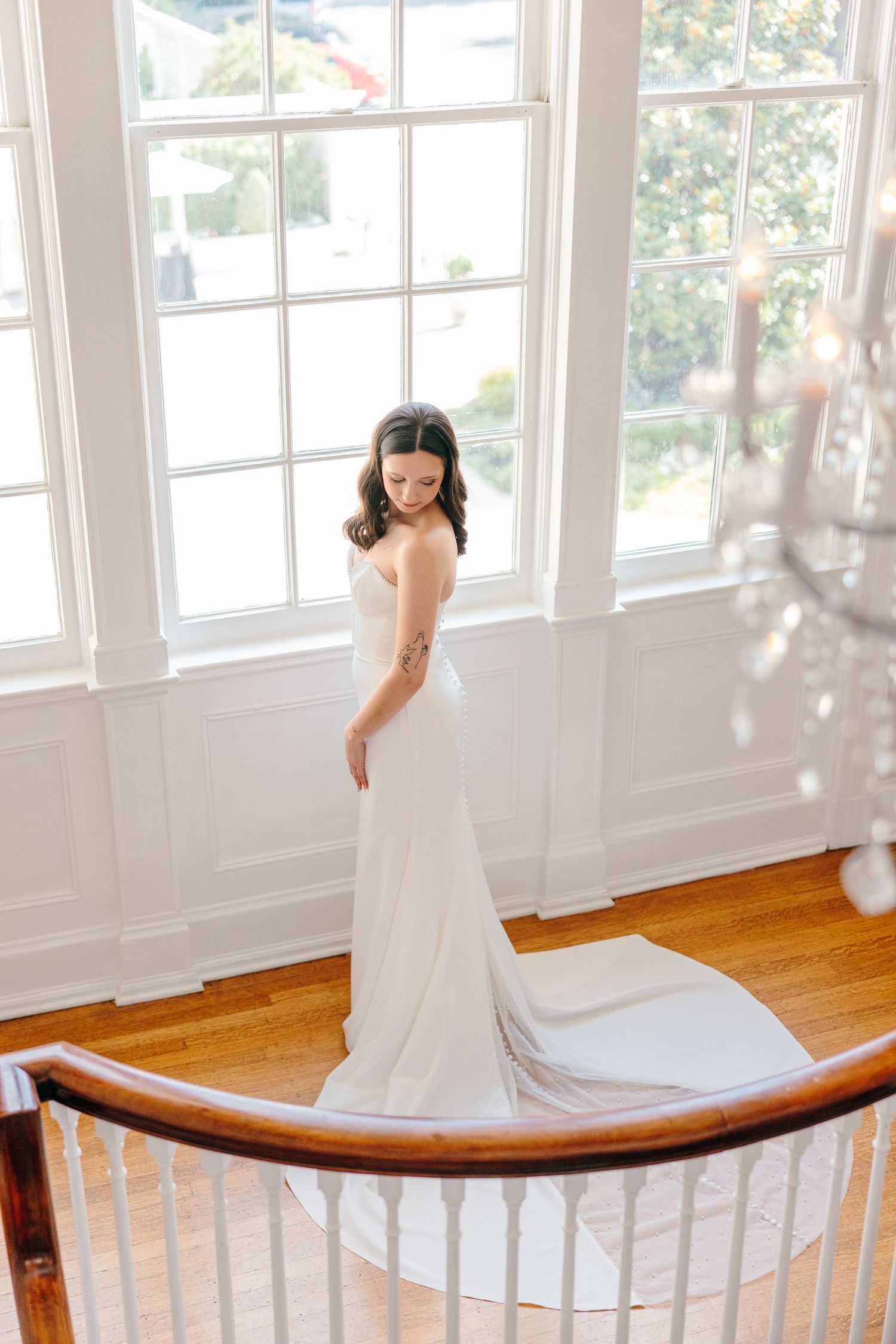 Elegant white wedding dress flowing across a curved wooden banister in a sunlit room.