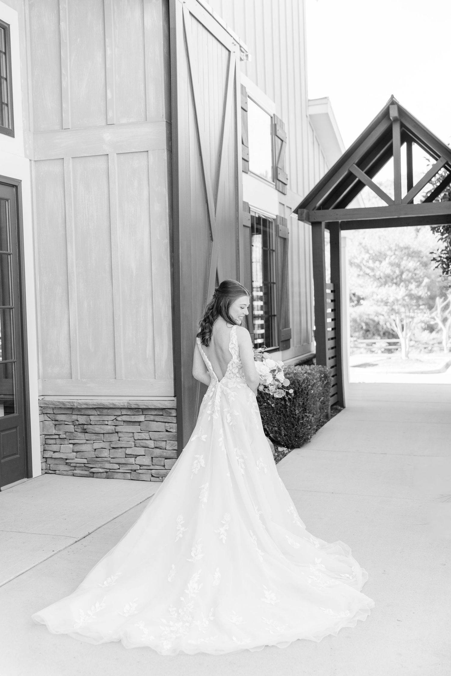 Elegant bride in flowing wedding gown with long train standing outside modern building.