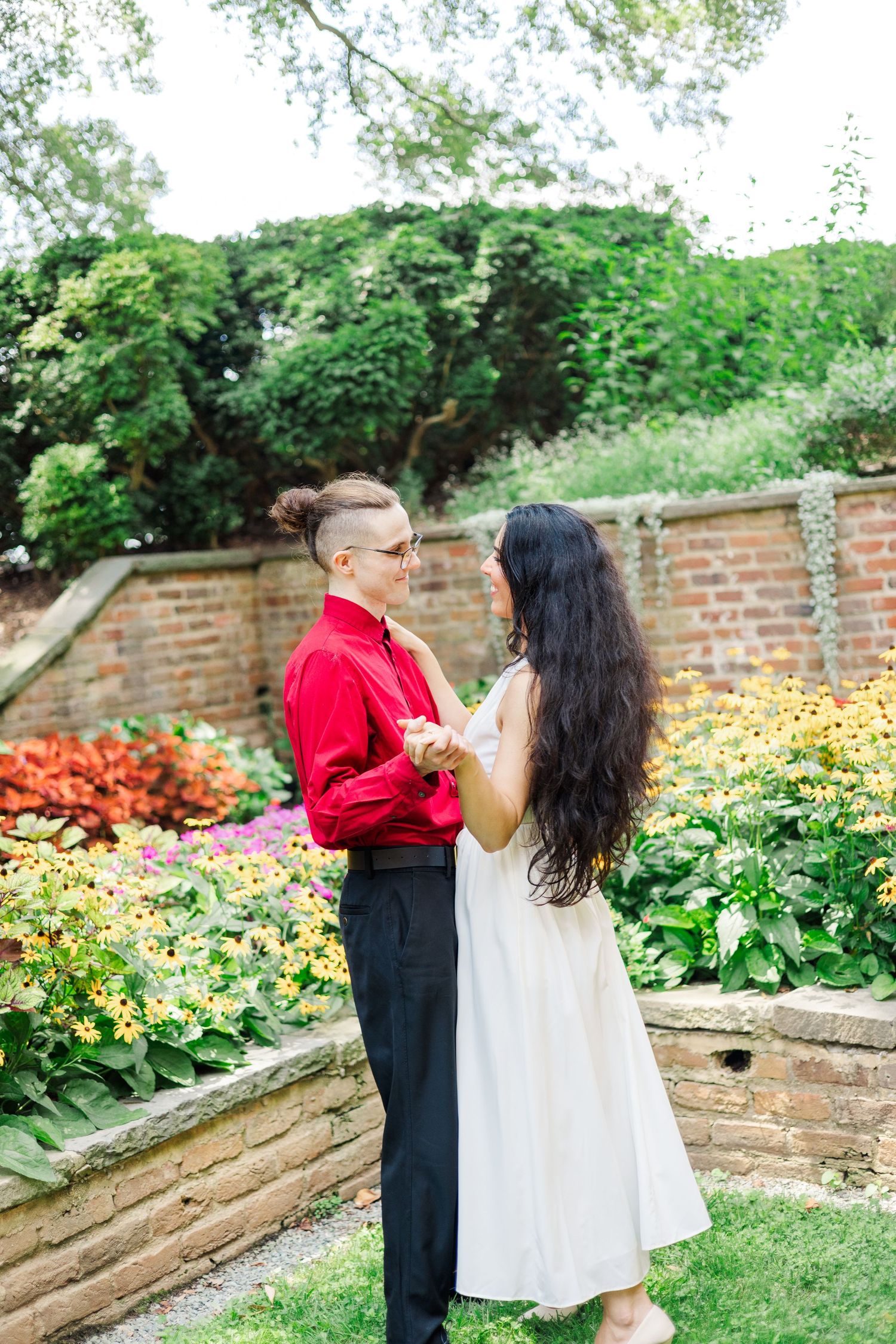 A couple shares romantic moments in a garden with brick walls and vibrant flowers.