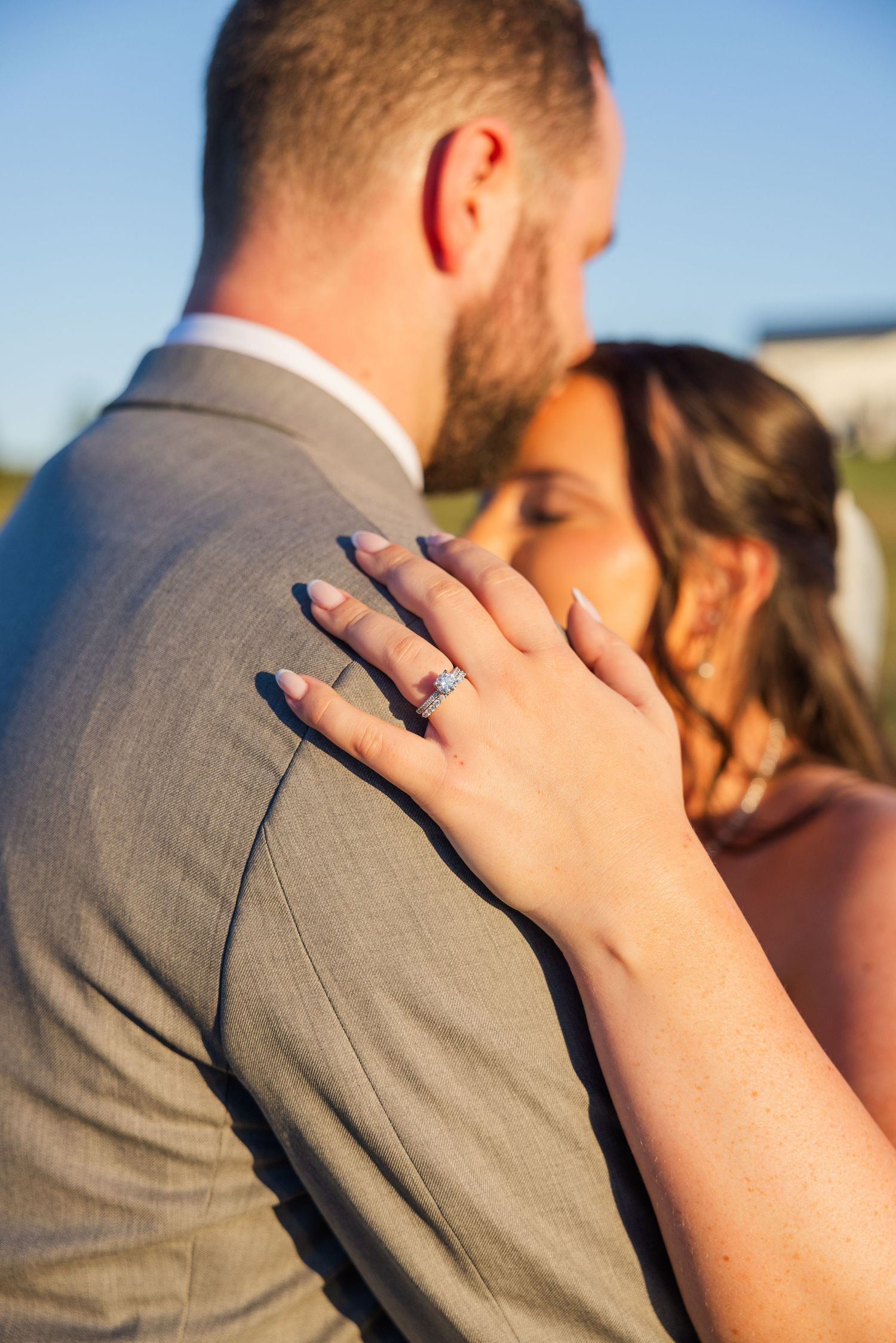 Close-up of an engagement ring as couple embraces during golden hour.