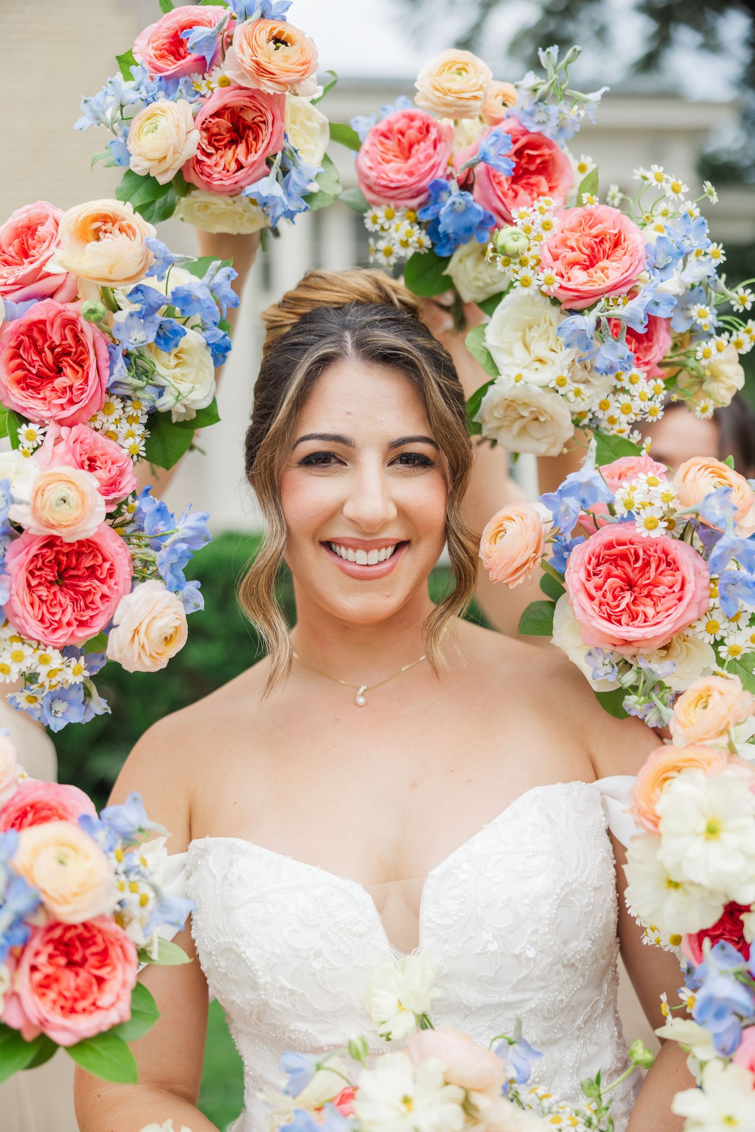 Beautiful floral arrangements featuring coral roses and blue delphinium frame a bridal portrait.