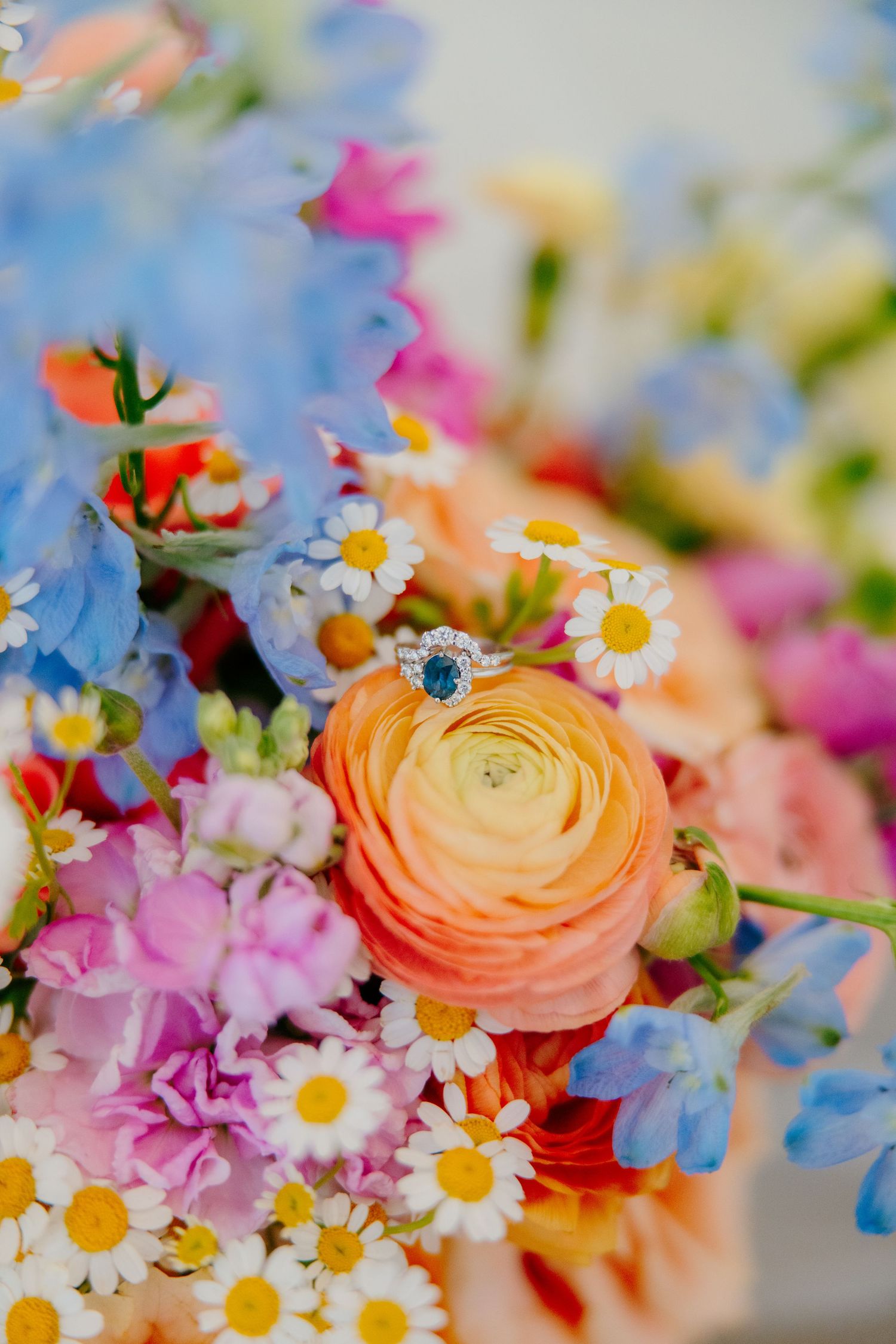 Colorful spring flowers including orange ranunculus, pink blooms, and white daisies arranged in a bright bouquet.