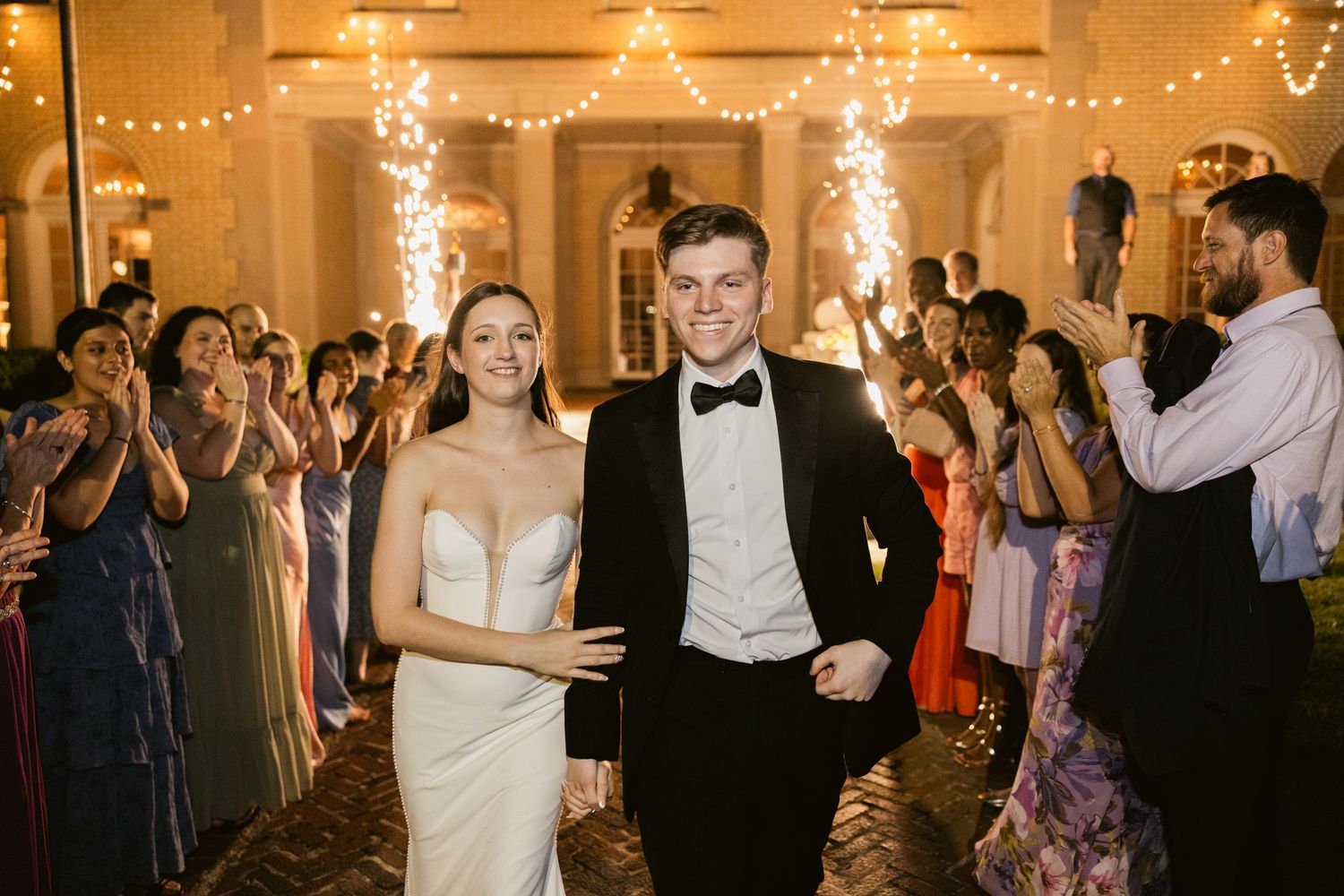 Wedding reception dance floor illuminated by warm string lights with guests celebrating.