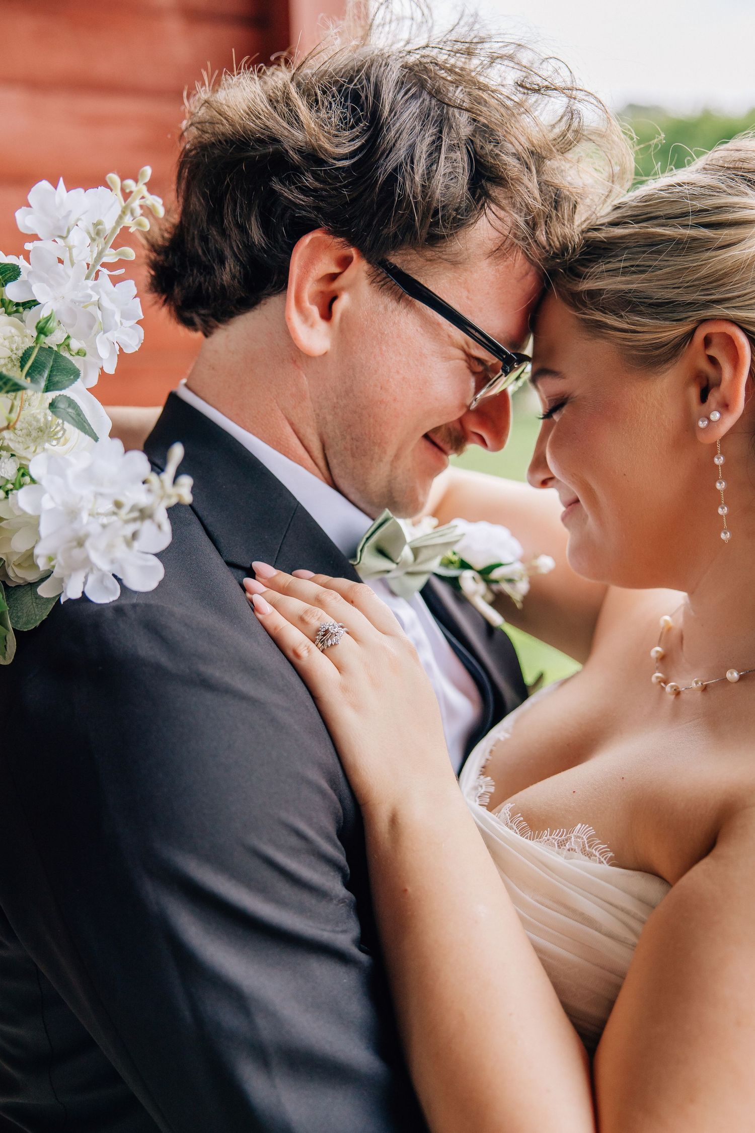 A joyful bride and groom share an intimate moment, touching foreheads and smiling, adorned in wedding attire with white floral boutonniere.