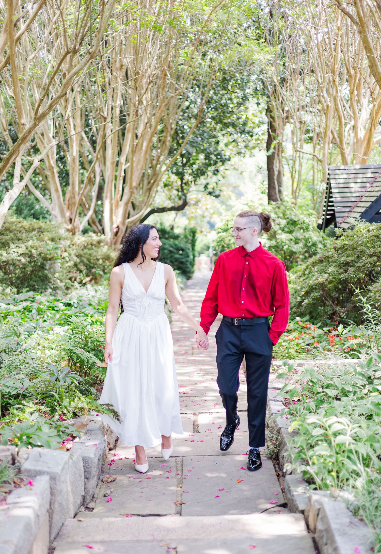 A couple walks hand in hand down stone garden steps surrounded by crepe myrtle trees.