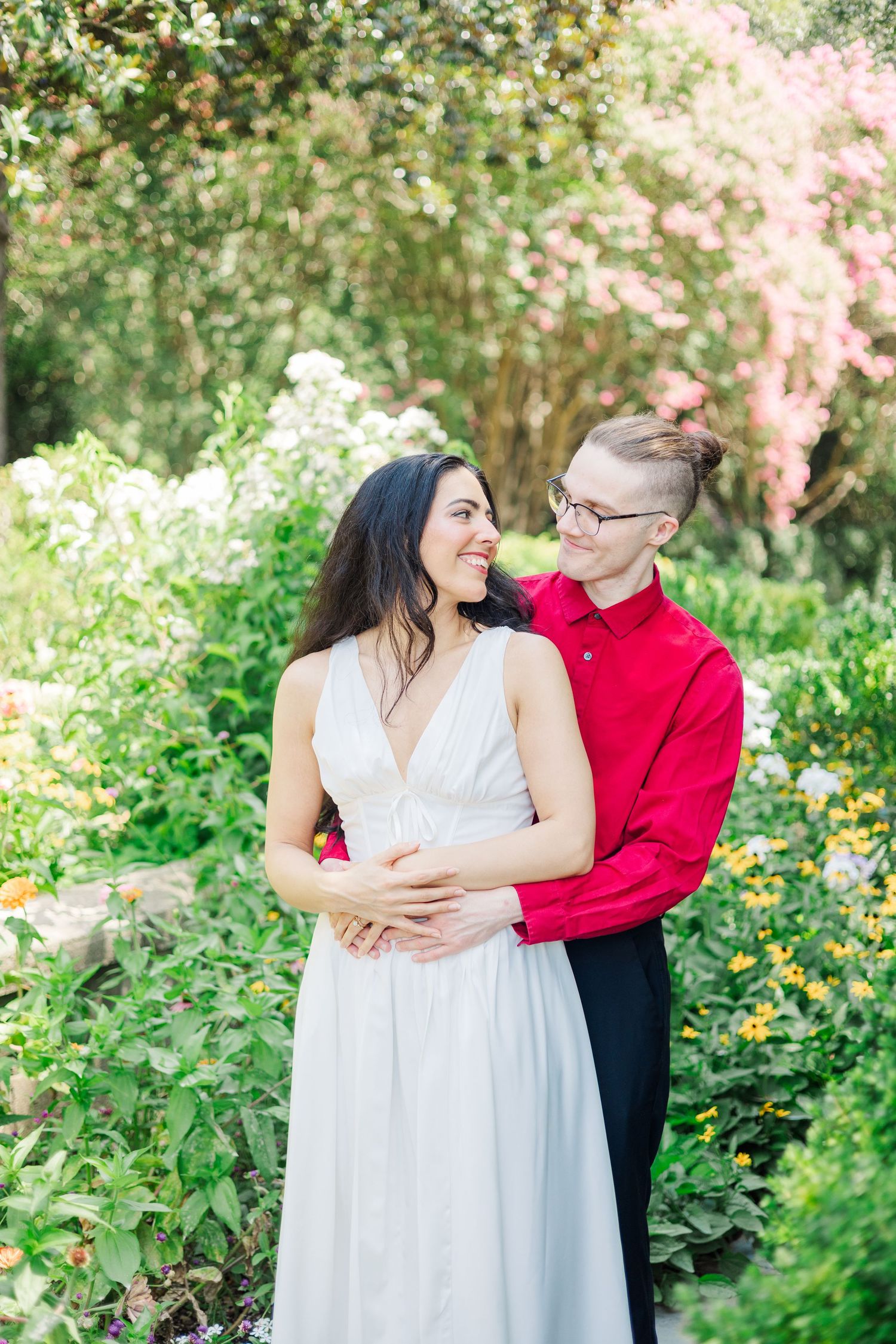A romantic couple embraces in a lush garden setting with blooming flowers and greenery.