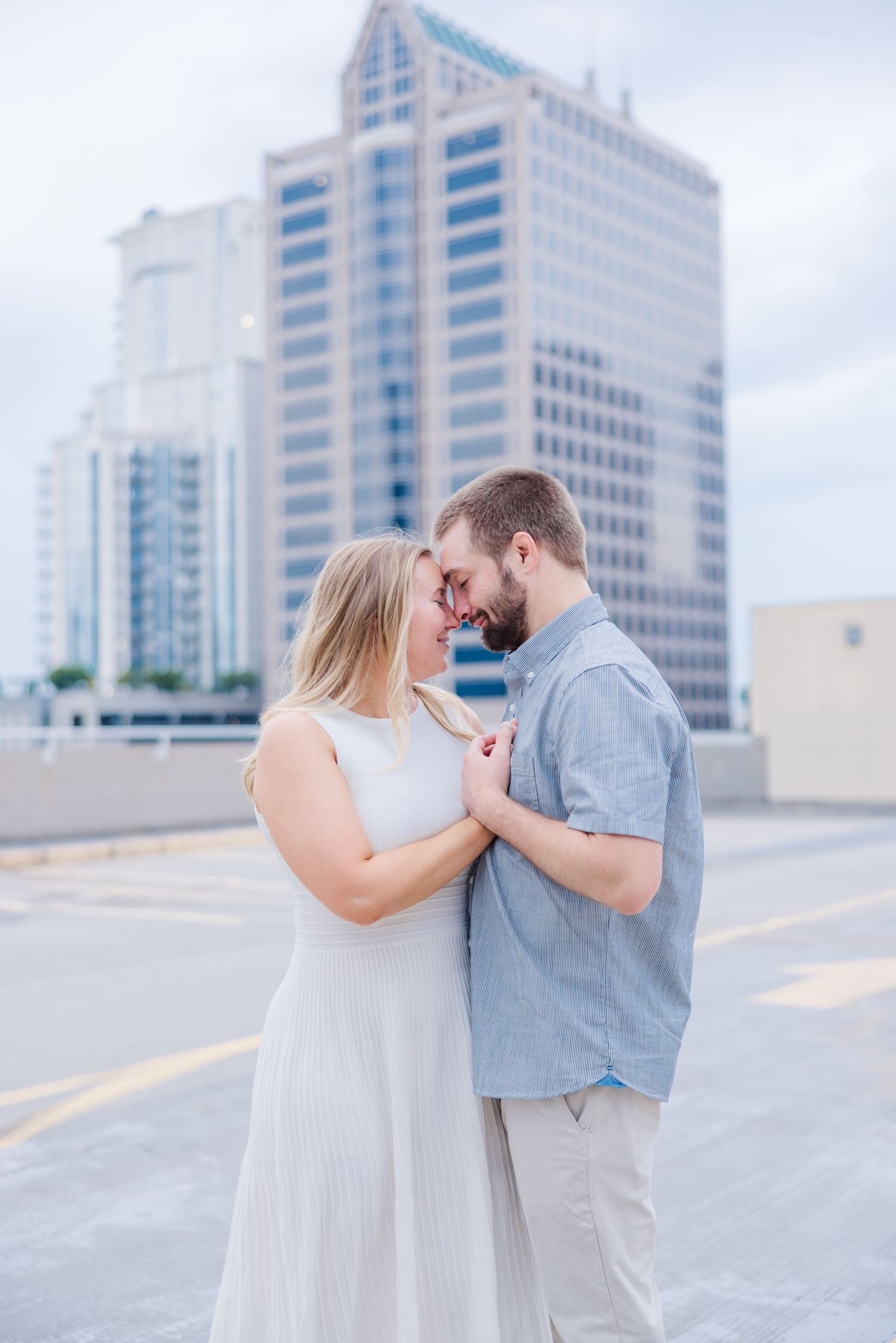 Couple shares romantic moment against modern city architecture during engagement session.