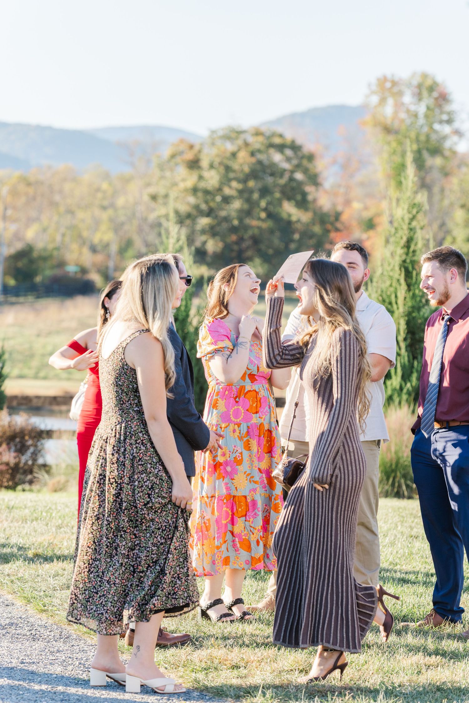Wedding guests in colorful dresses gathered outdoors with mountain backdrop at sunset.