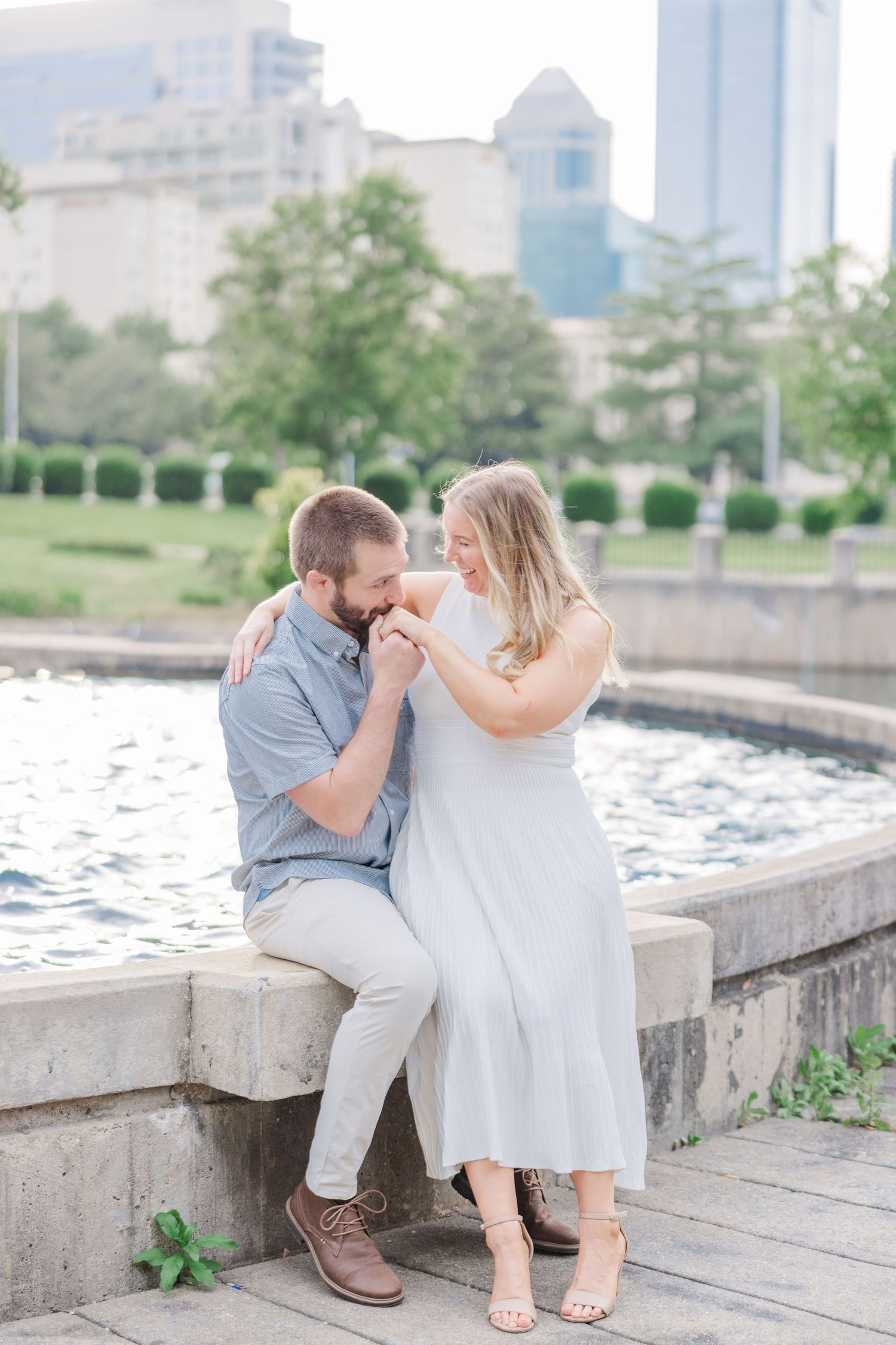 Couple shares intimate moment while sitting on concrete wall near waterfront during golden hour.