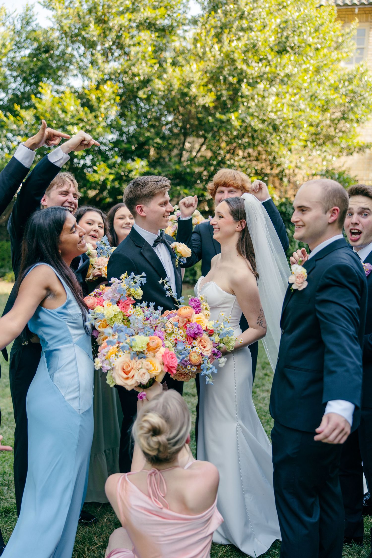 Wedding party celebrates outdoors with colorful bouquets and joyful expressions during a summer celebration.