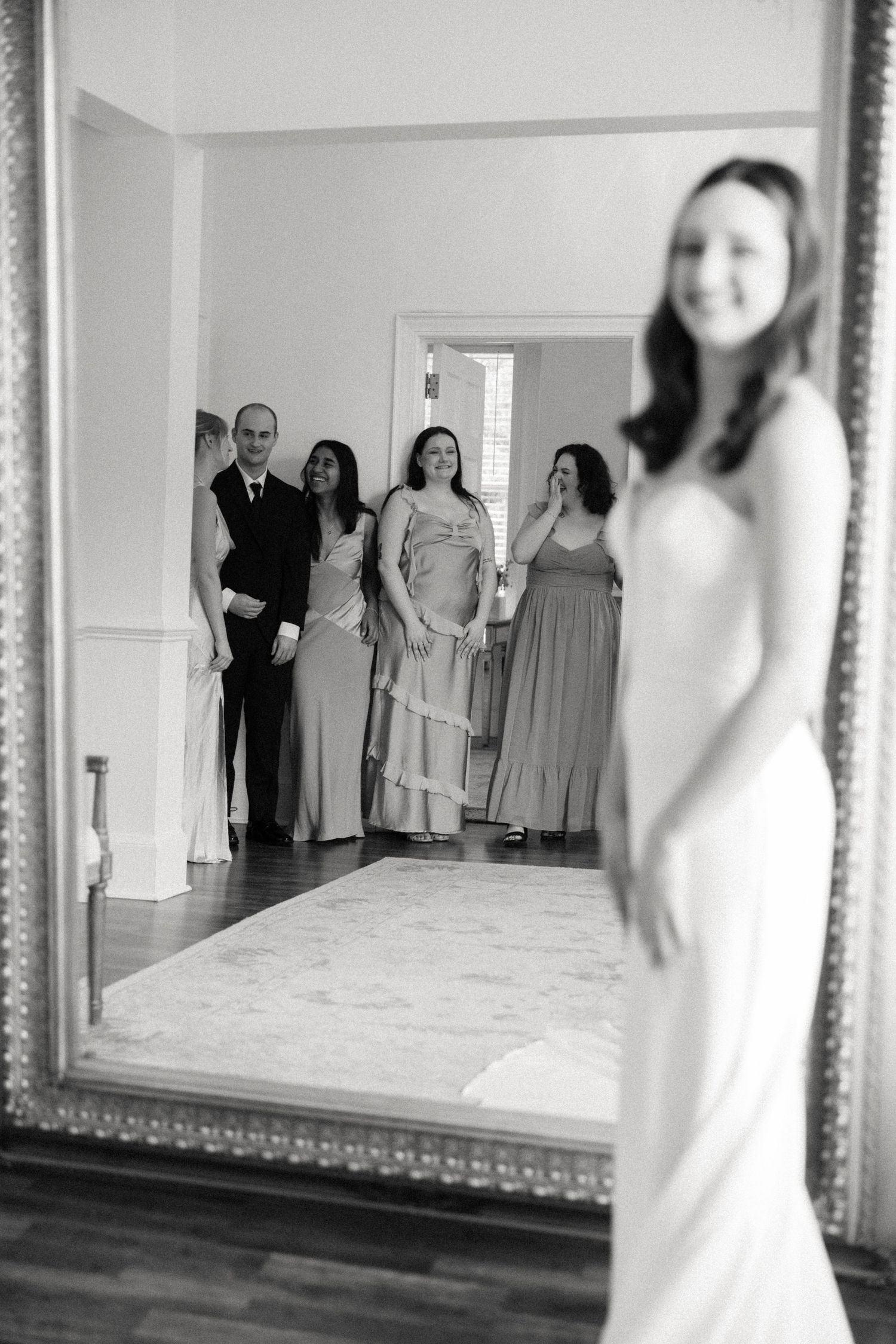 A black and white wedding photo showing a reflection of a bridal party in an elegant framed mirror.