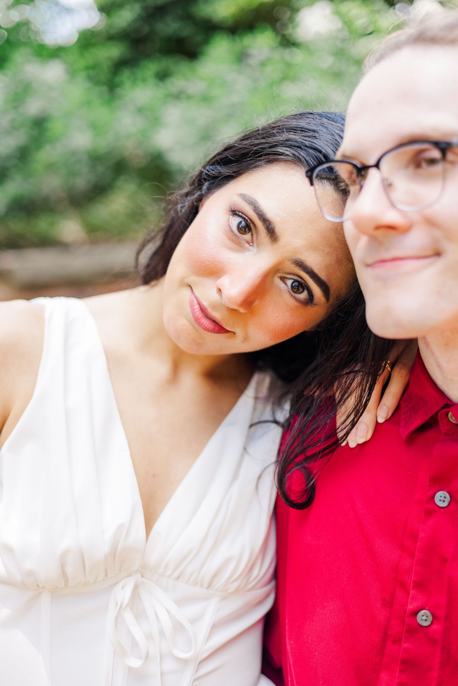 A couple poses for intimate close-up portraits against a soft natural background with trees.
