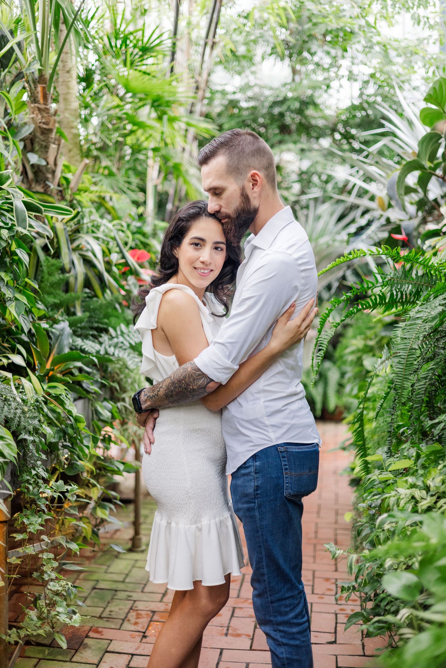 Romantic greenhouse photoshoot with couple surrounded by lush tropical plants.