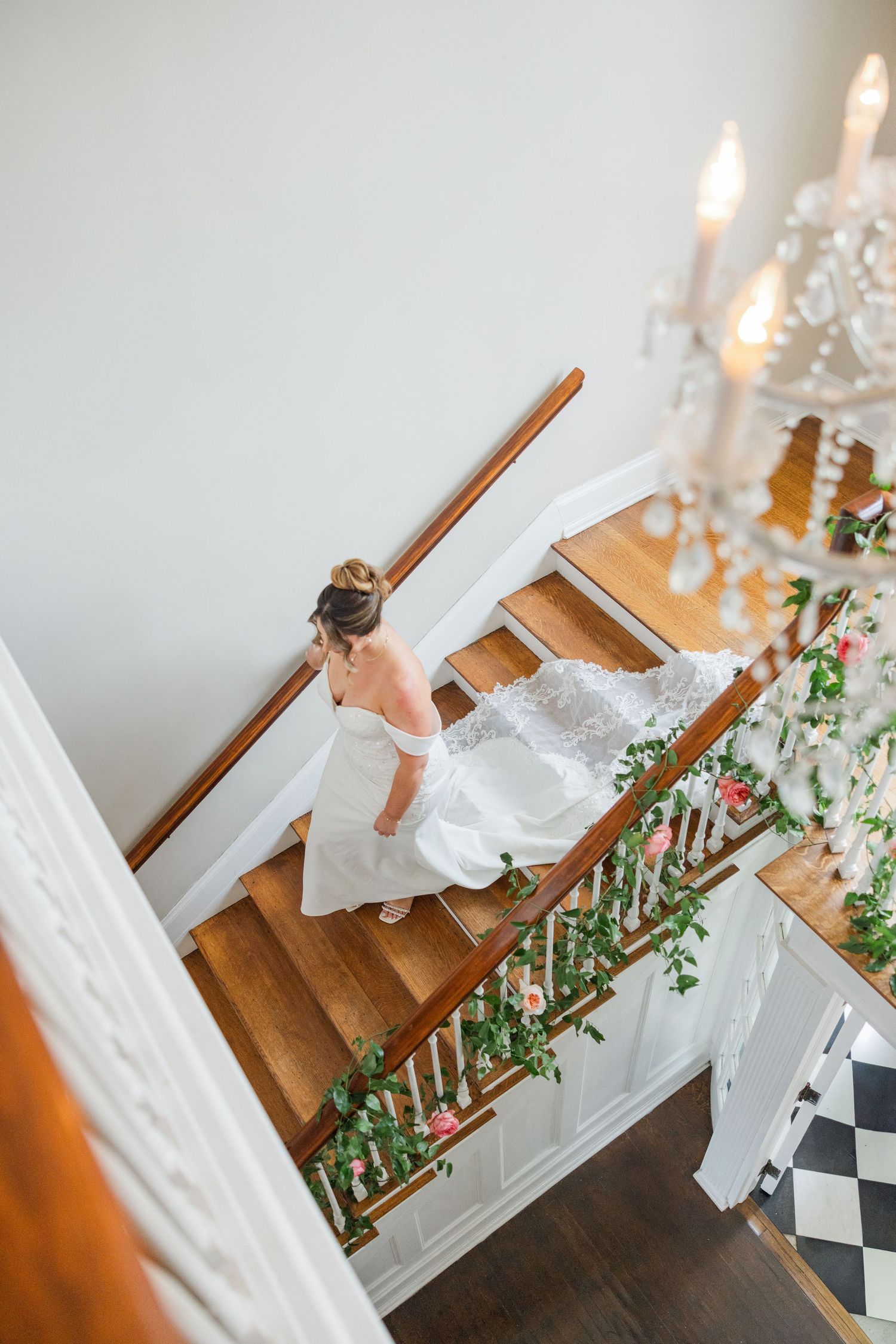 Bride descending elegant staircase decorated with greenery and candles.