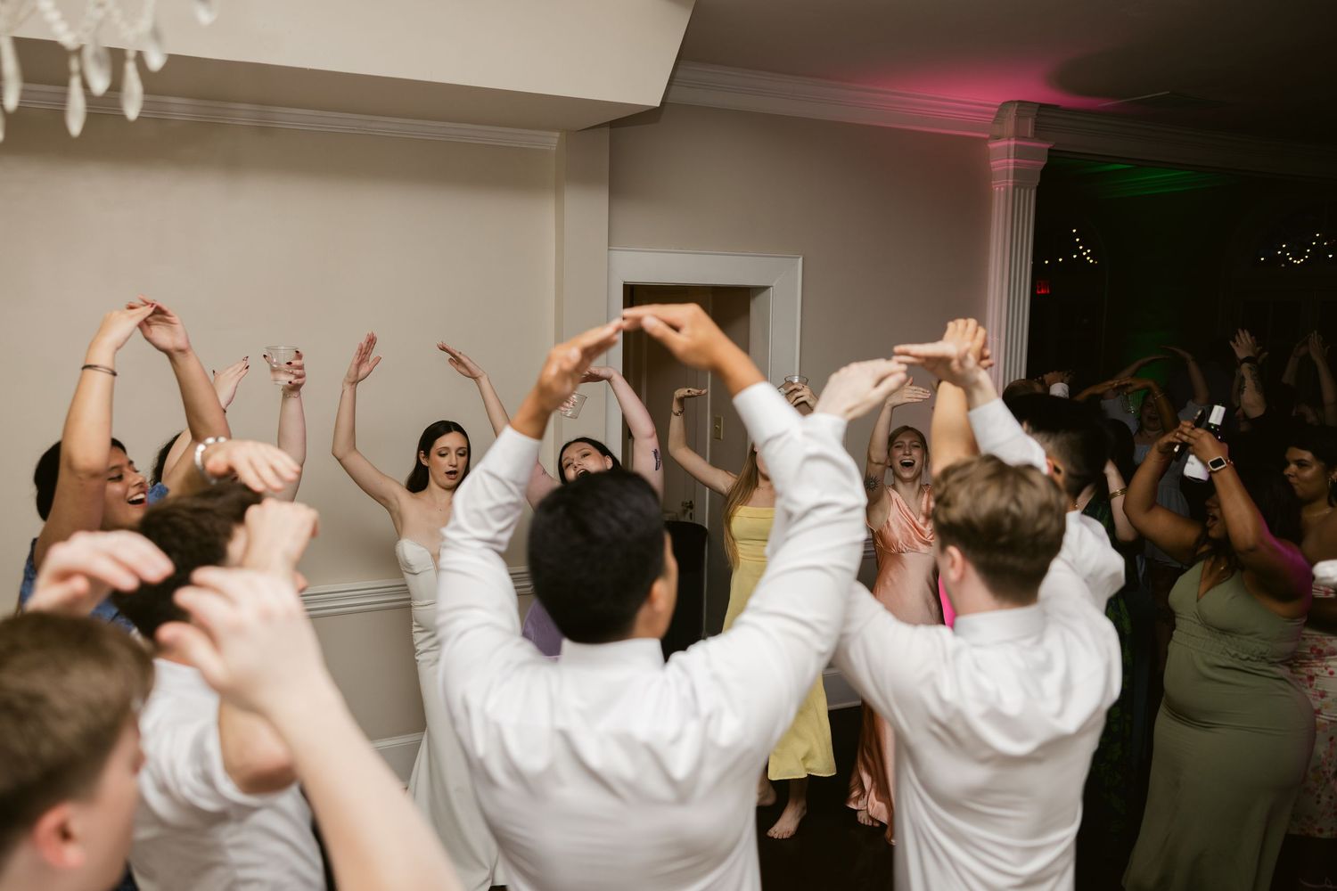 Wedding reception dance floor filled with guests raising their hands in celebration.