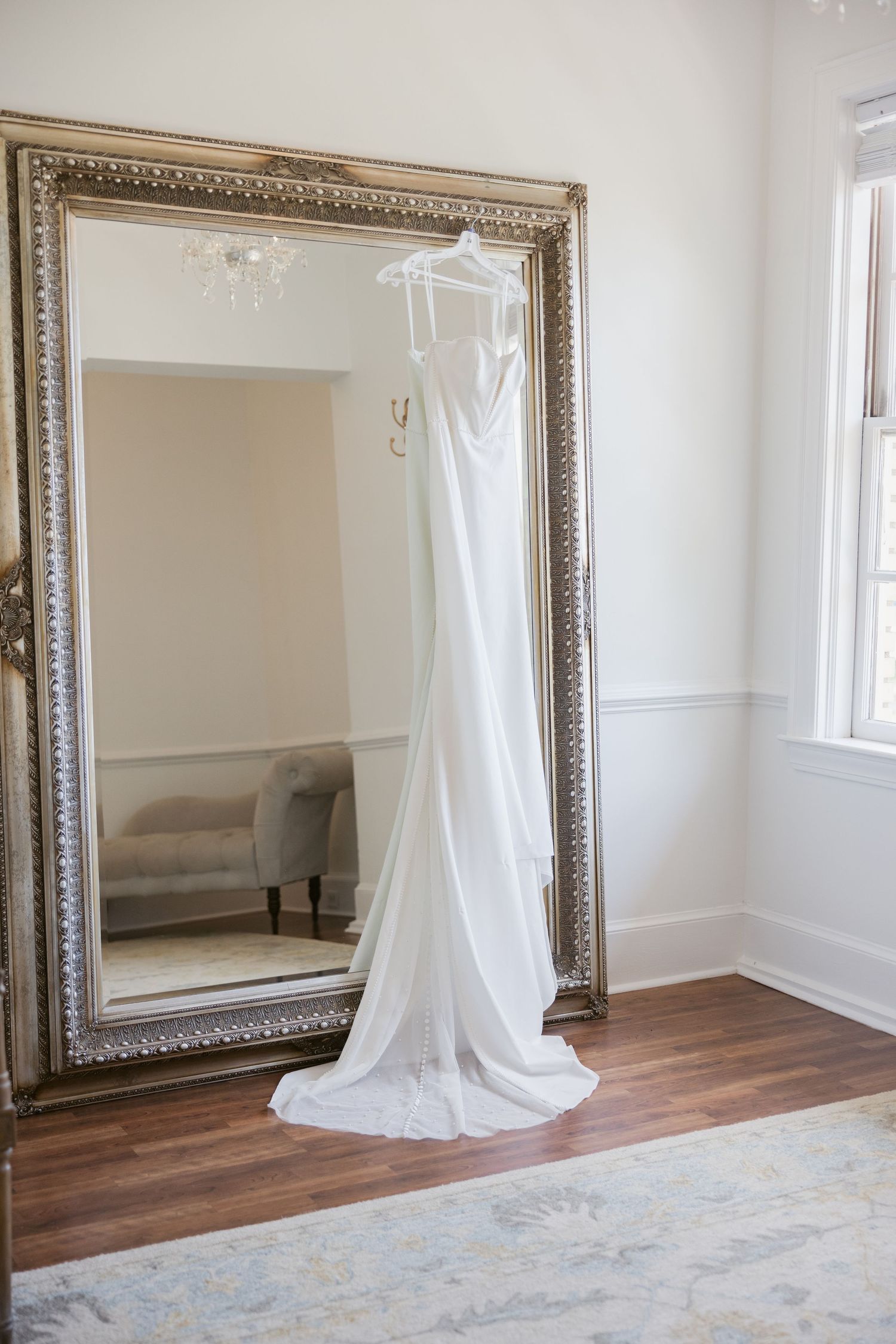 Empty room interior with hardwood floors, white walls, and an ornate framed mirror.
