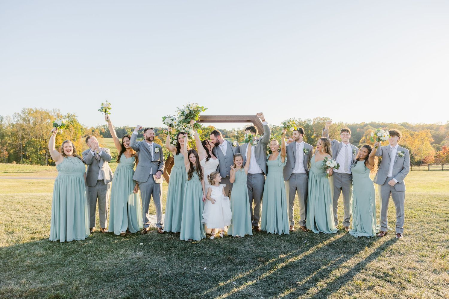 Large wedding party in coordinated blue and gray outfits poses together outdoors.