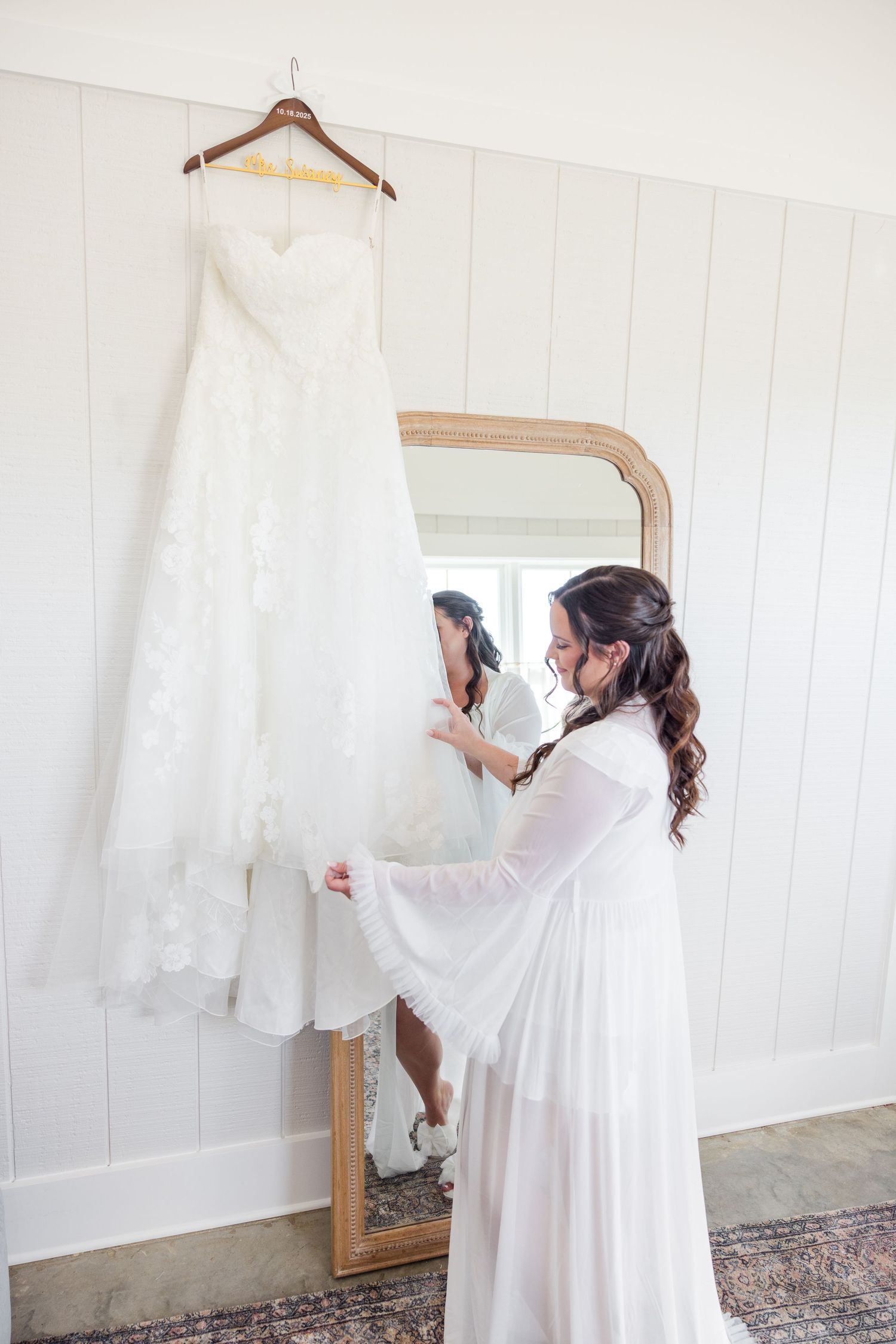 White wedding dress being prepared and hung on wooden hangers against a white wall.