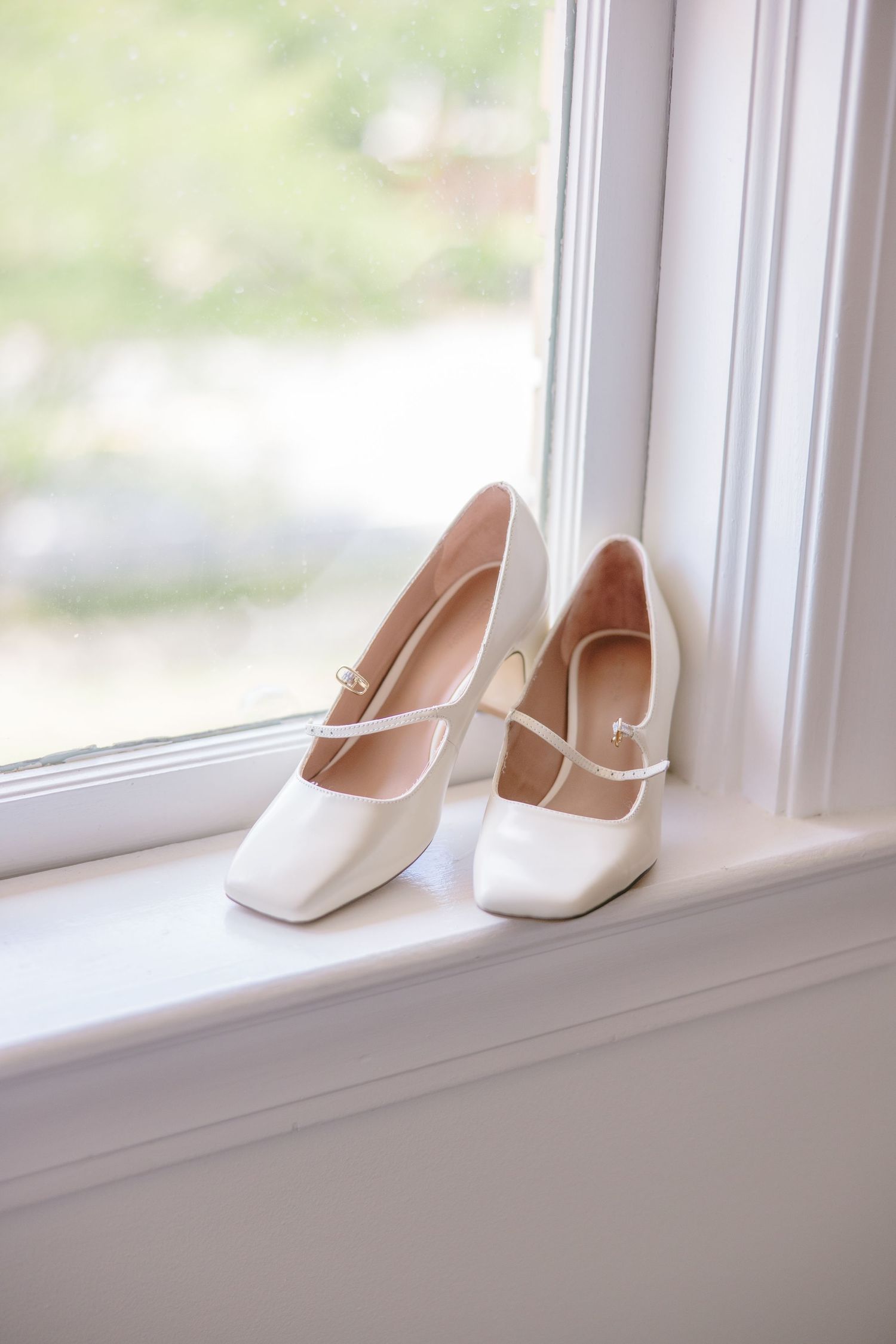 Classic white bridal shoes displayed on a windowsill with natural lighting.